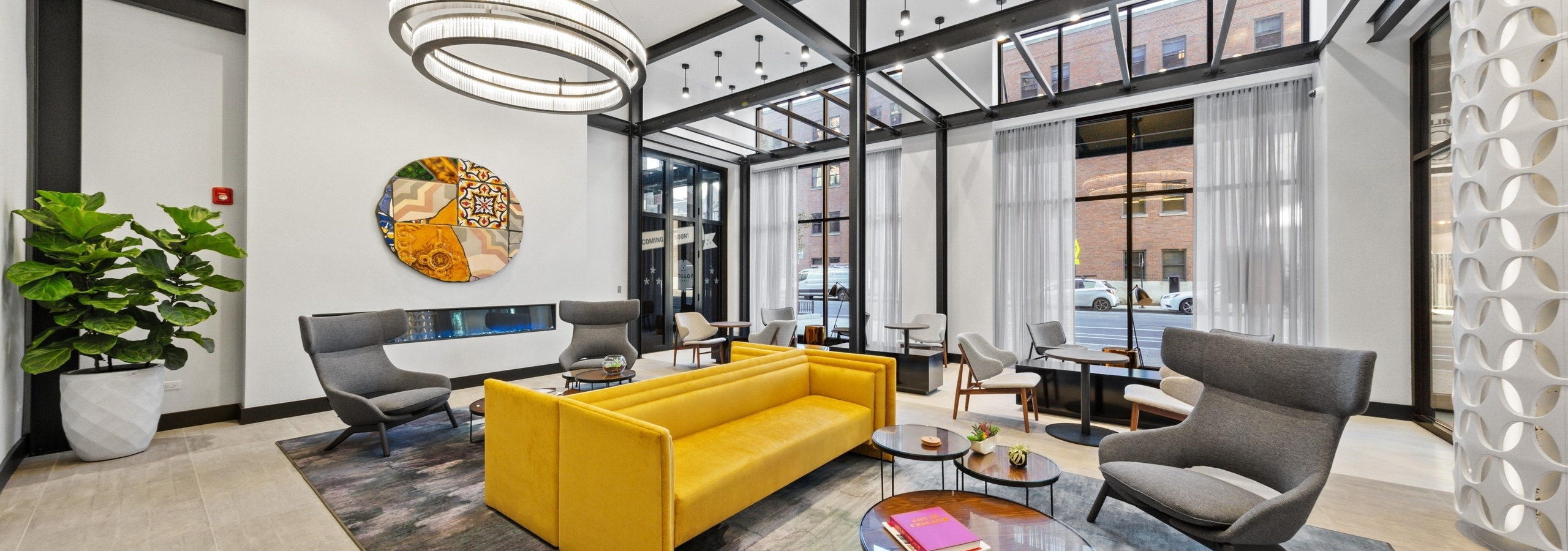 AMLI 808 lobby with bold yellow couches and grey chairs surrounded by floor to ceiling windows and modern light fixtures