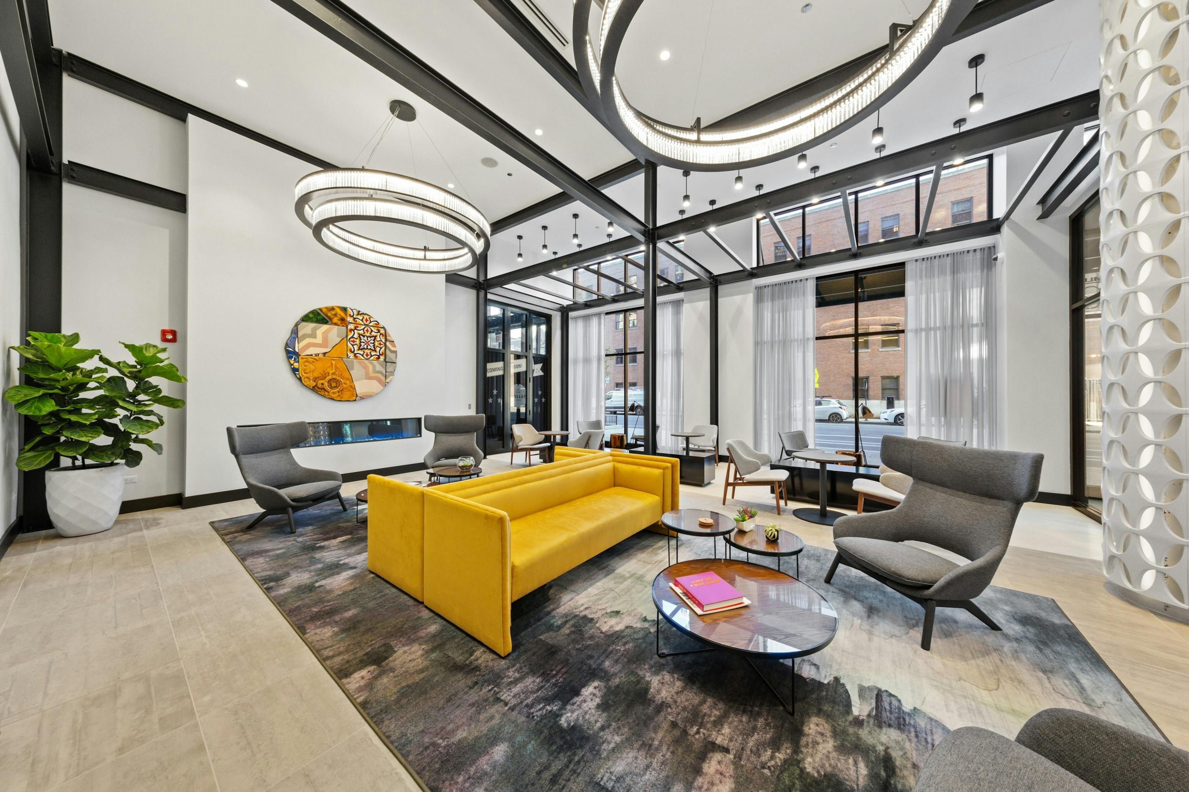 AMLI 808 lobby with bold yellow couches and grey chairs surrounded by floor to ceiling windows and modern light fixtures