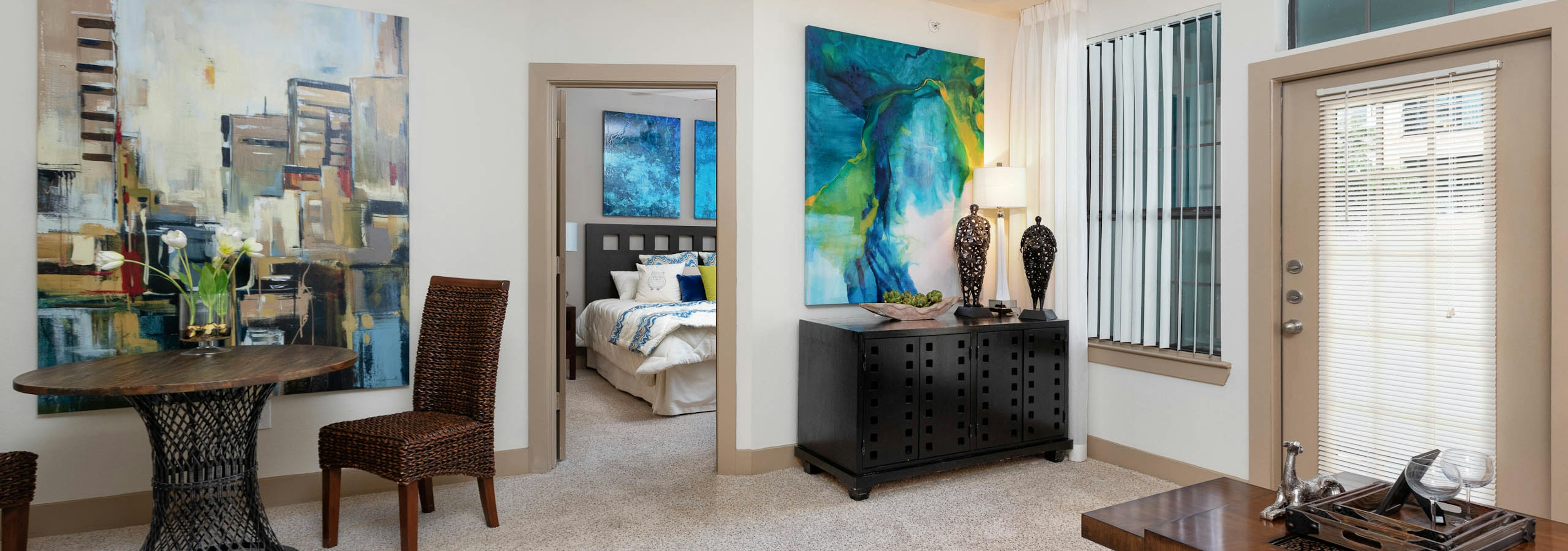 Carpeted dining area at AMLI Eastside with a small dark table with two chairs and a peek into bedroom through an open door