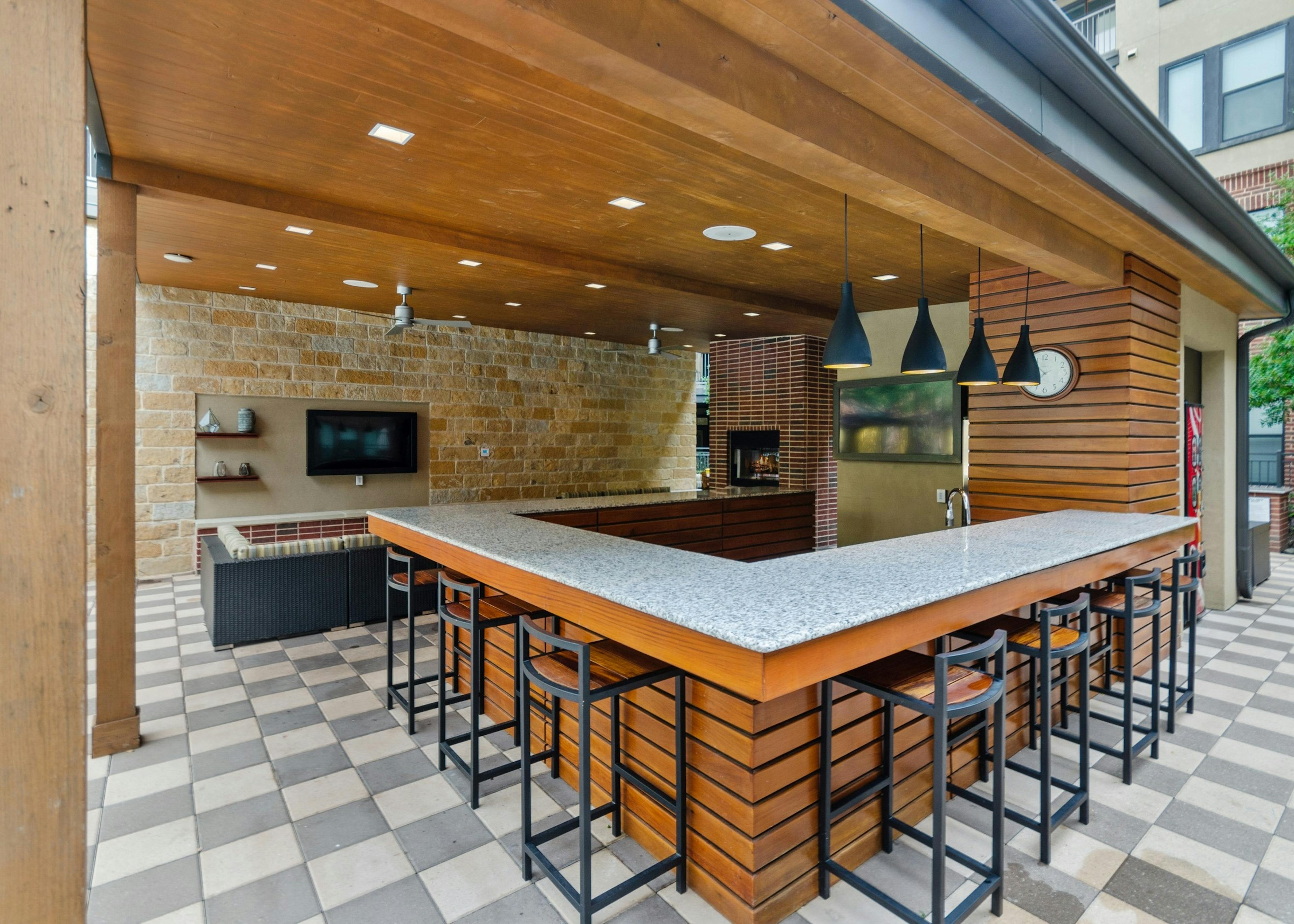 Outdoor covered kitchen at AMLI West Plano apartments surrounded by gray countertops and bar seating with large TVs