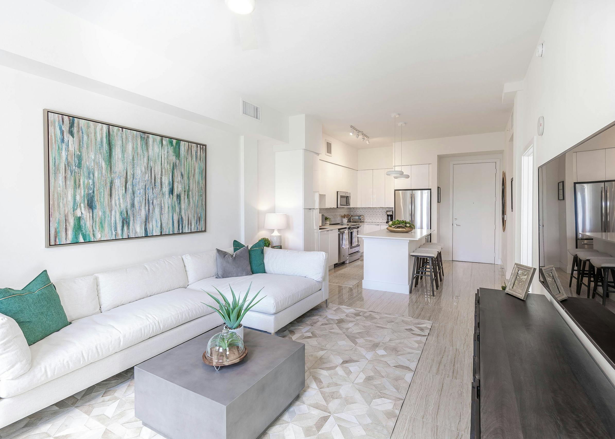 AMLI Park West apartments living area with white sofa with  green abstract art above and a view into the white island kitchen