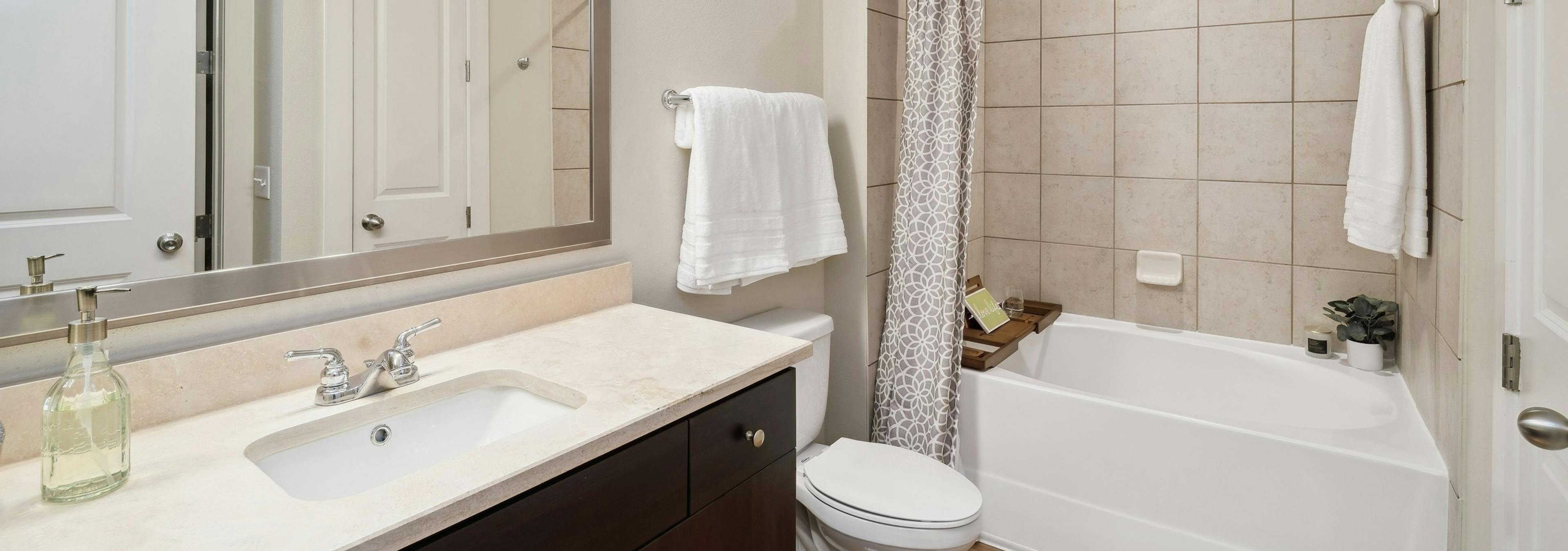 An apartment bathroom at AMLI RidgeGate with a tub/shower with tile surround and wood vanity with mirror above