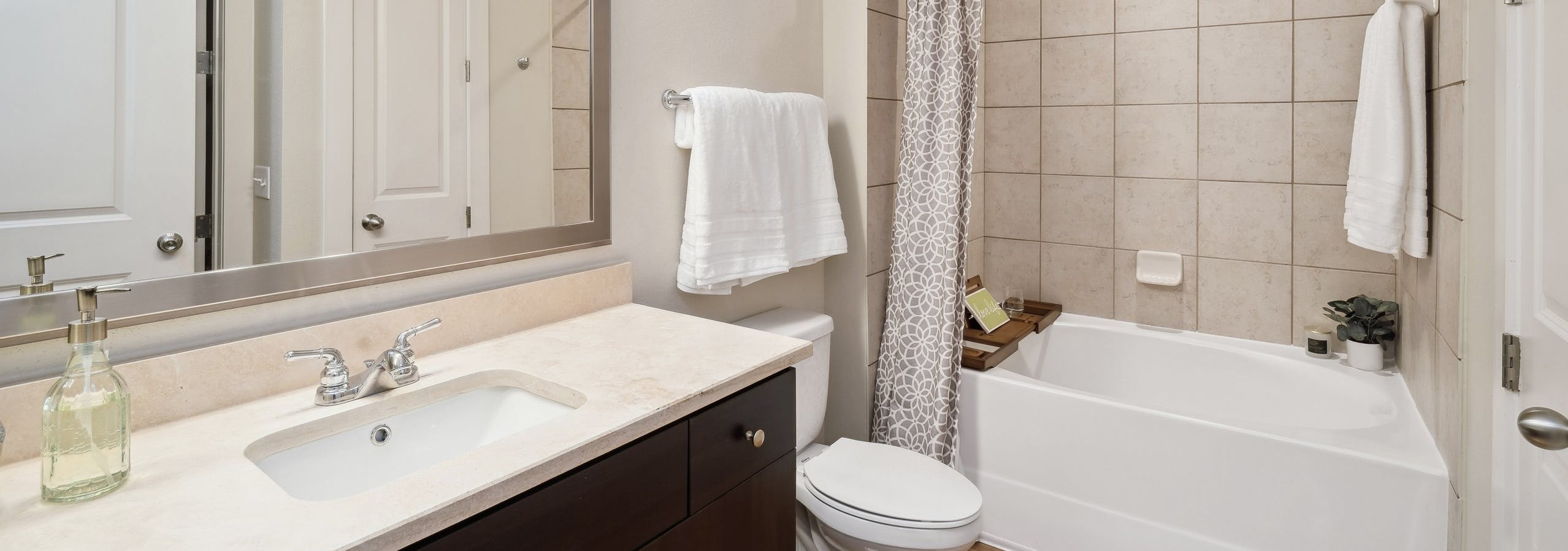 An apartment bathroom at AMLI RidgeGate with a tub/shower with tile surround and wood vanity with mirror above