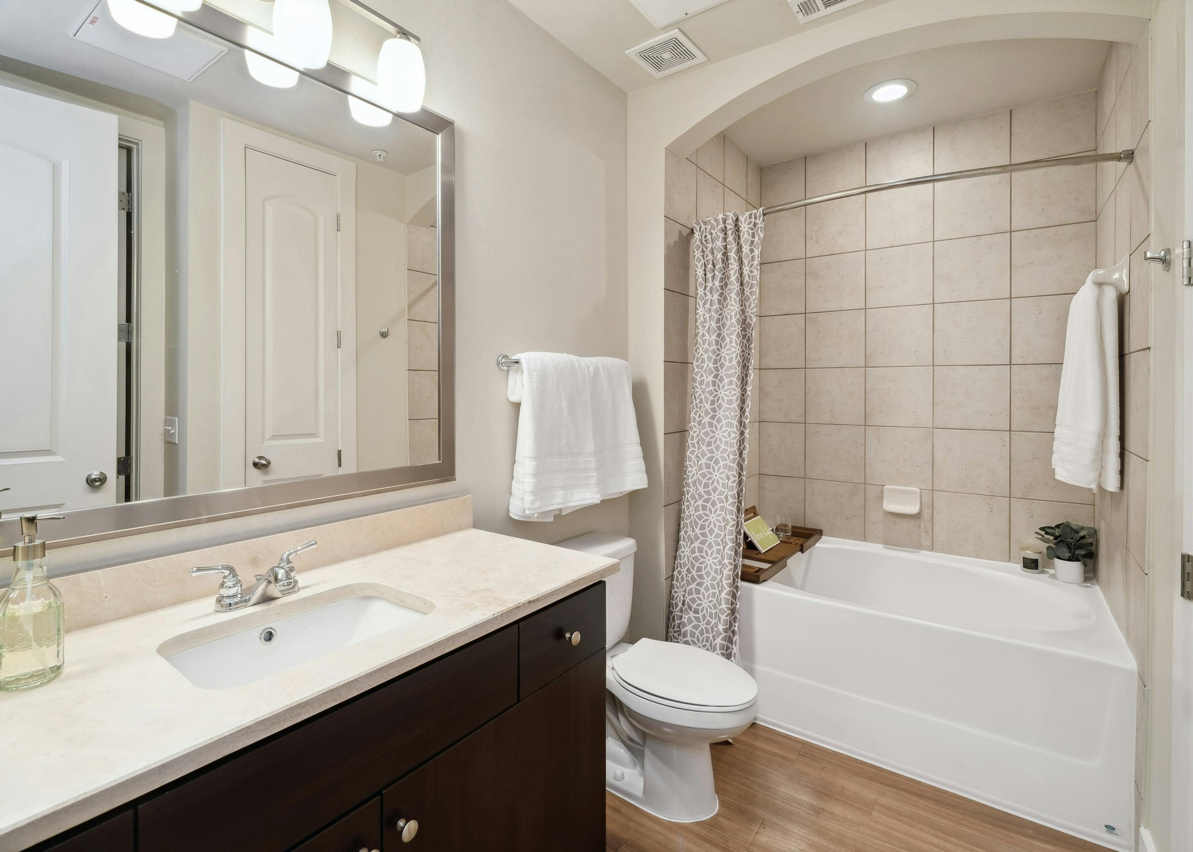 An apartment bathroom at AMLI RidgeGate with a tub/shower with tile surround and wood vanity with mirror above