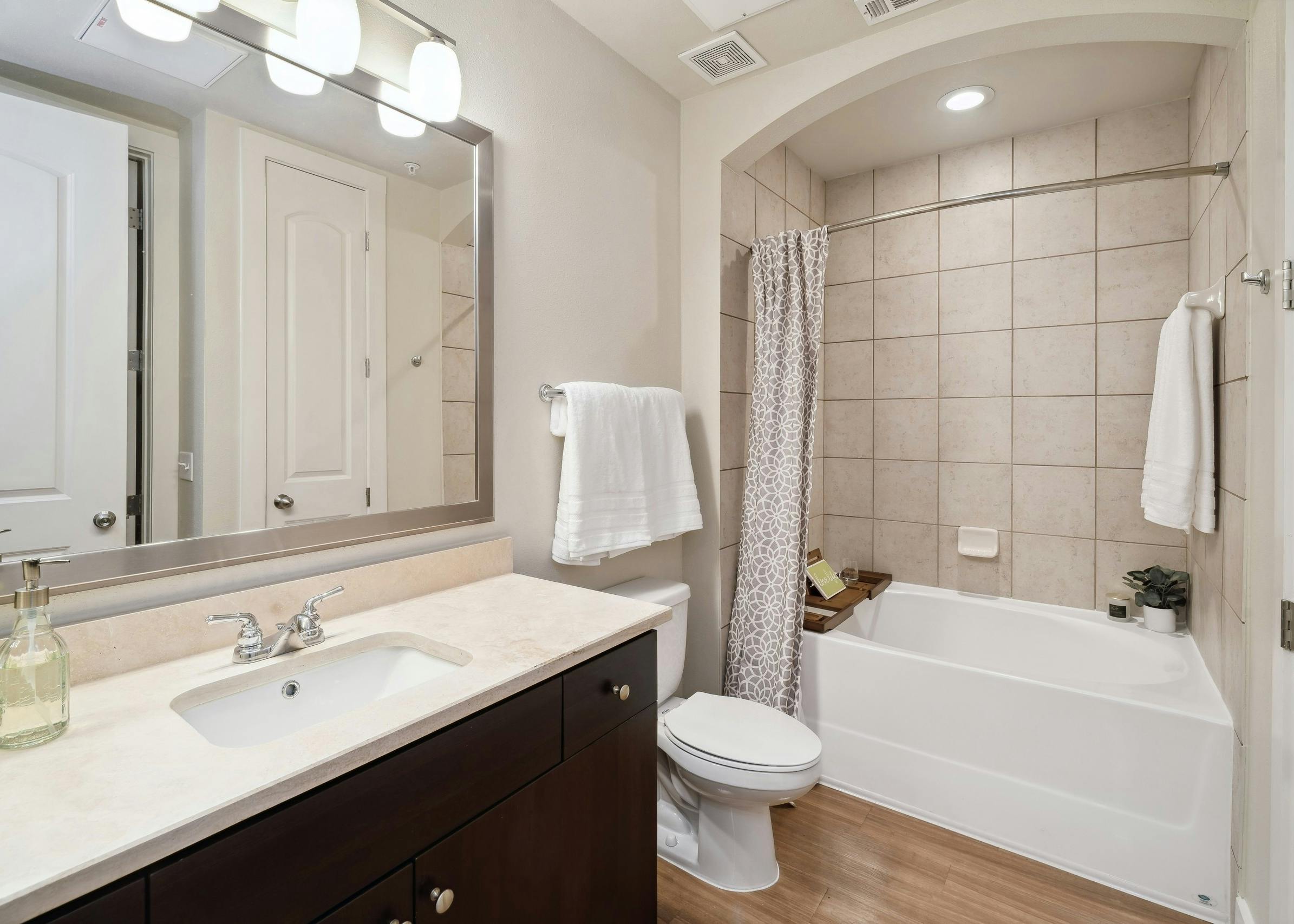 An apartment bathroom at AMLI RidgeGate with a tub/shower with tile surround and wood vanity with mirror above