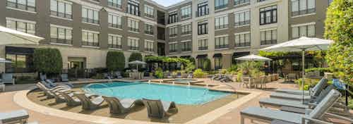 Daytime view of AMLI Las Colinas large courtyard pool surrounded by lounge seating with 3 umbrellas and lush landscaping