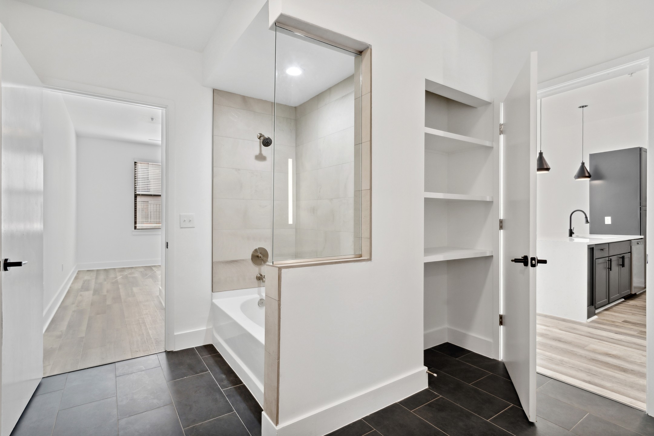 AMLI Old 4th Ward bathroom with a cream tiled shower/tub surround and shelved storage nook with view to bedroom and kitchen 