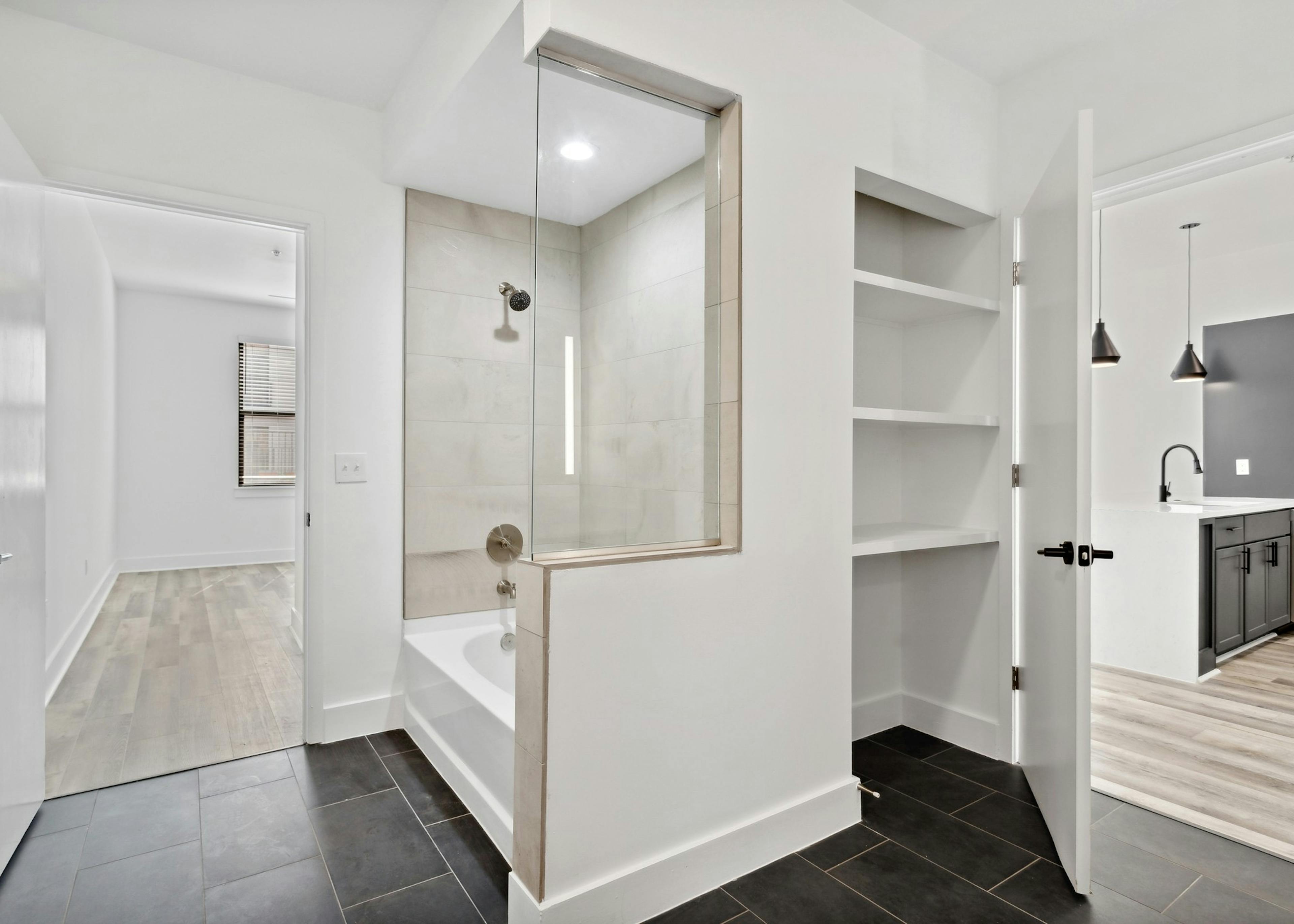 AMLI Old 4th Ward bathroom with a cream tiled shower/tub surround and shelved storage nook with view to bedroom and kitchen 