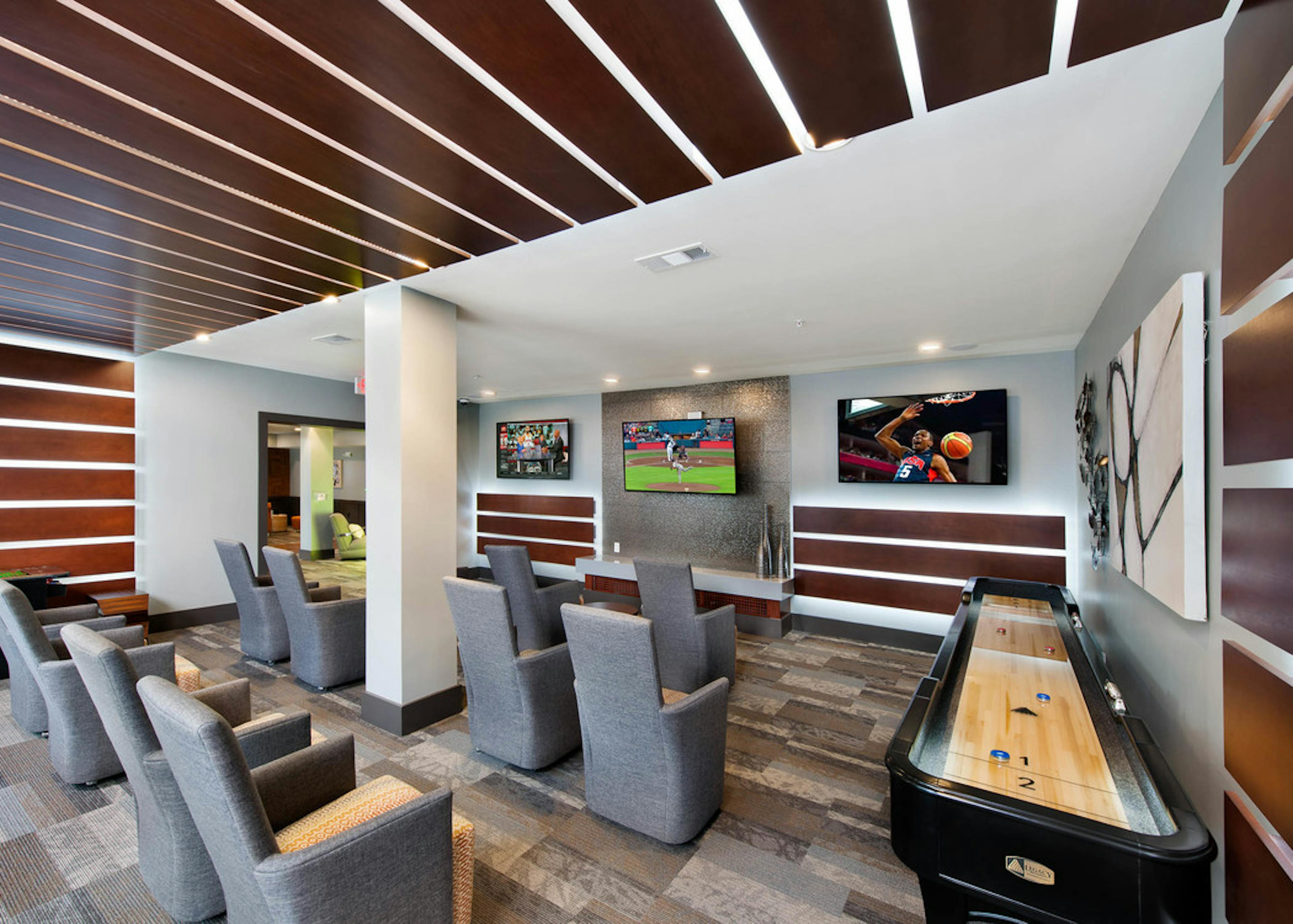 Interior view of the media room at AMLI Piedmont Heights with grey seating facing multiple large TVs on the wall 