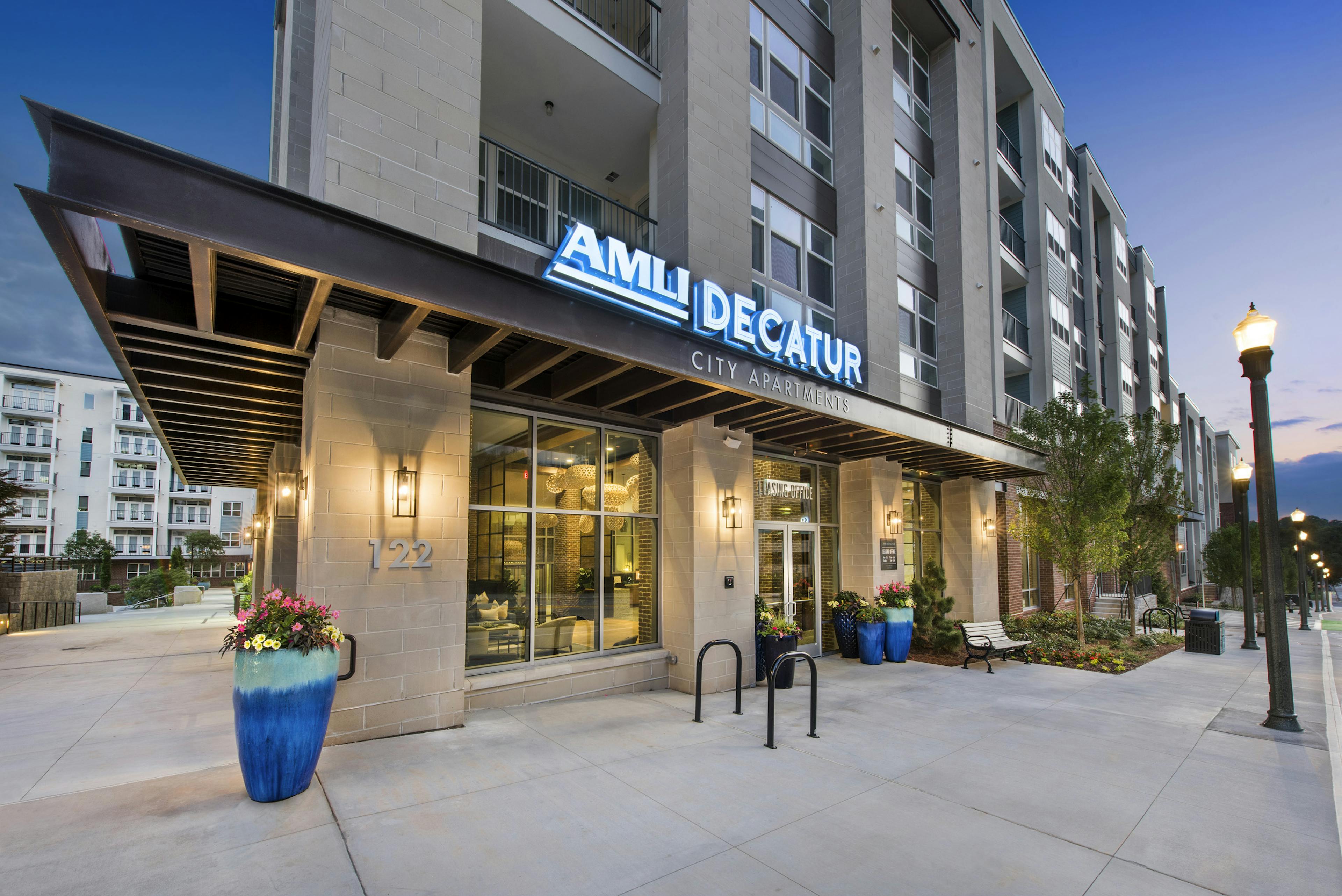 Evening view of AMLI Decatur signage lit in bright blue and white colors with lamp posts and trees lining the building