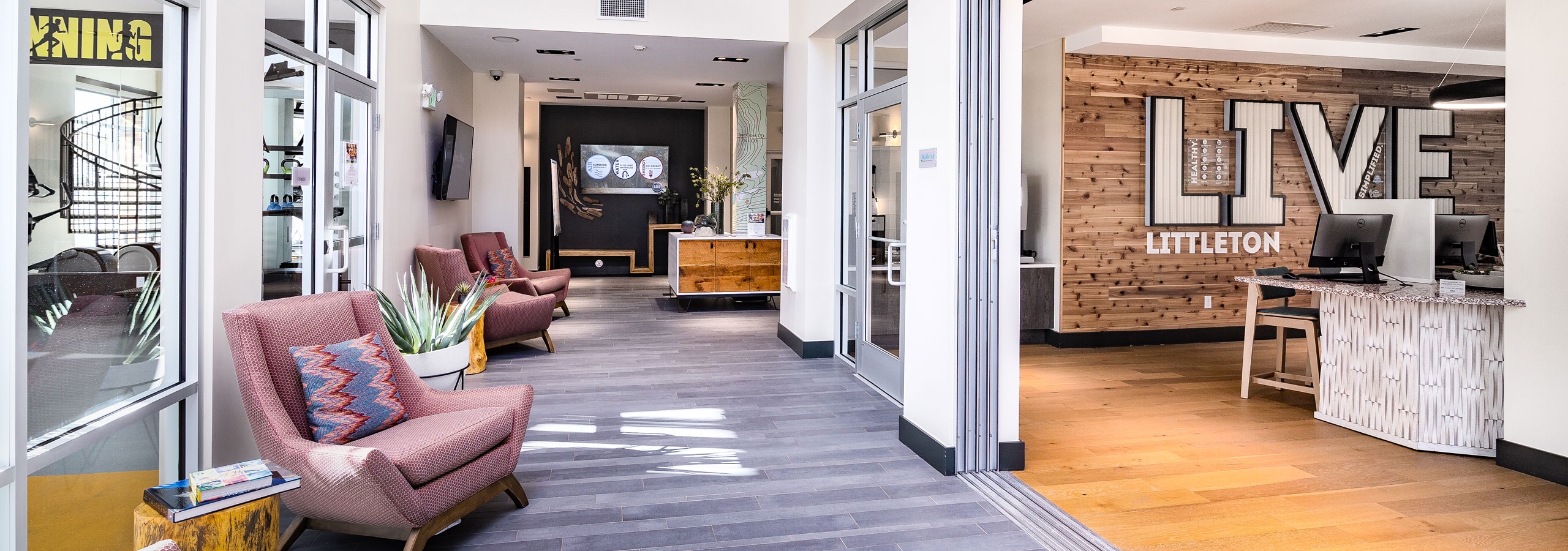 Interior of AML Littleton Village lobby with computer stations, wood paneling accent wall, lounge seating and big screen TV