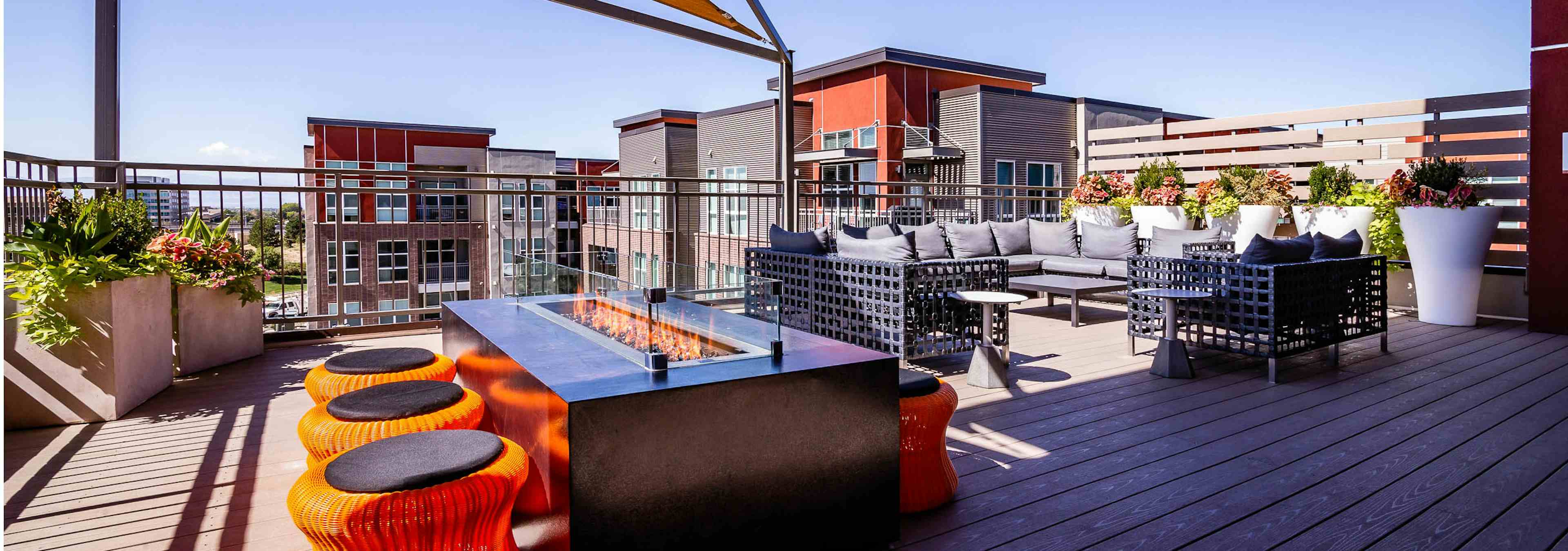 View of the rooftop at AMLI Dry Creek apartments with a fire pit and surrounding short stools as well as a sectional couch 