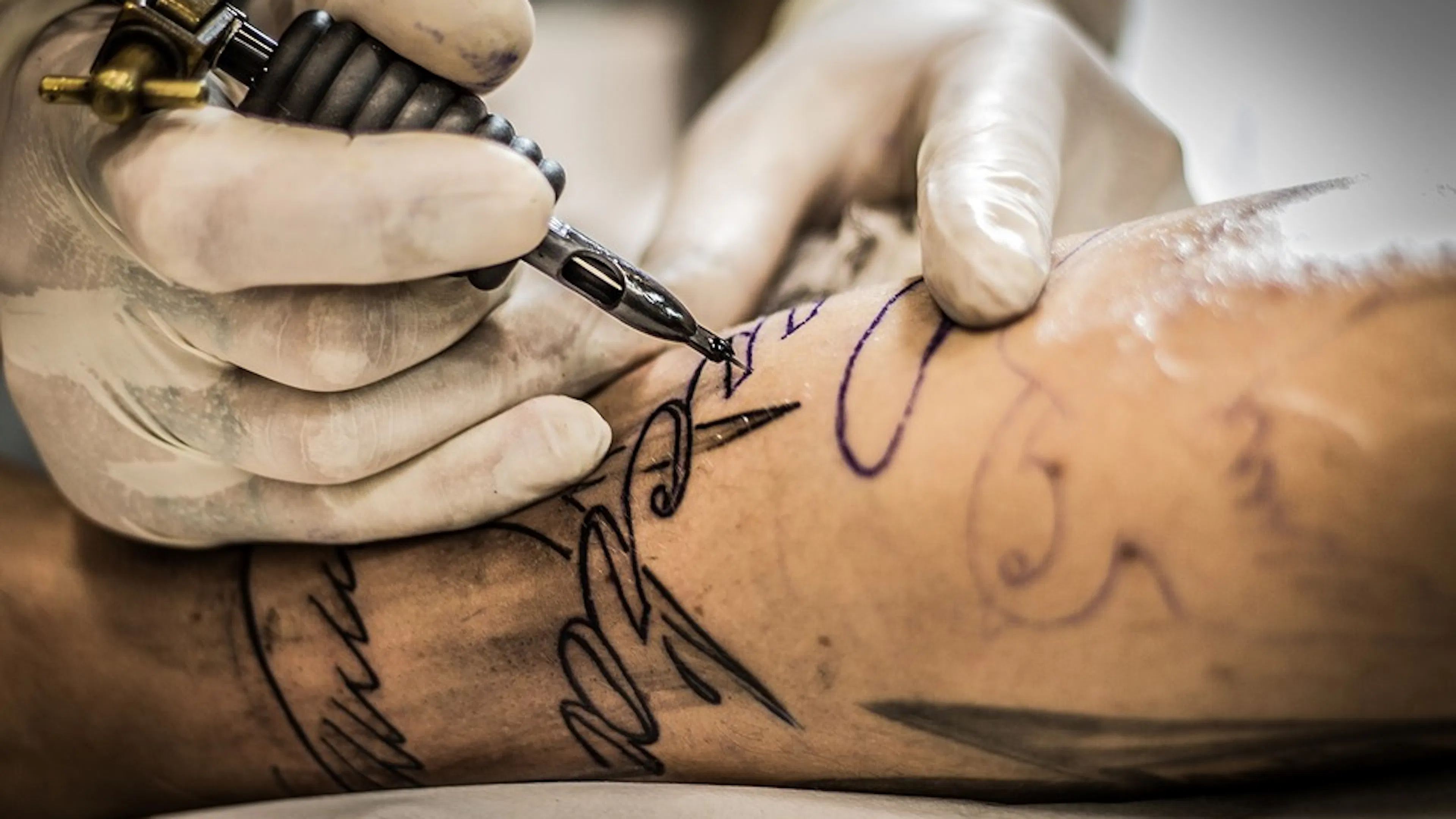 A tattoo artist tattooing a name onto an arm in fine black ink
