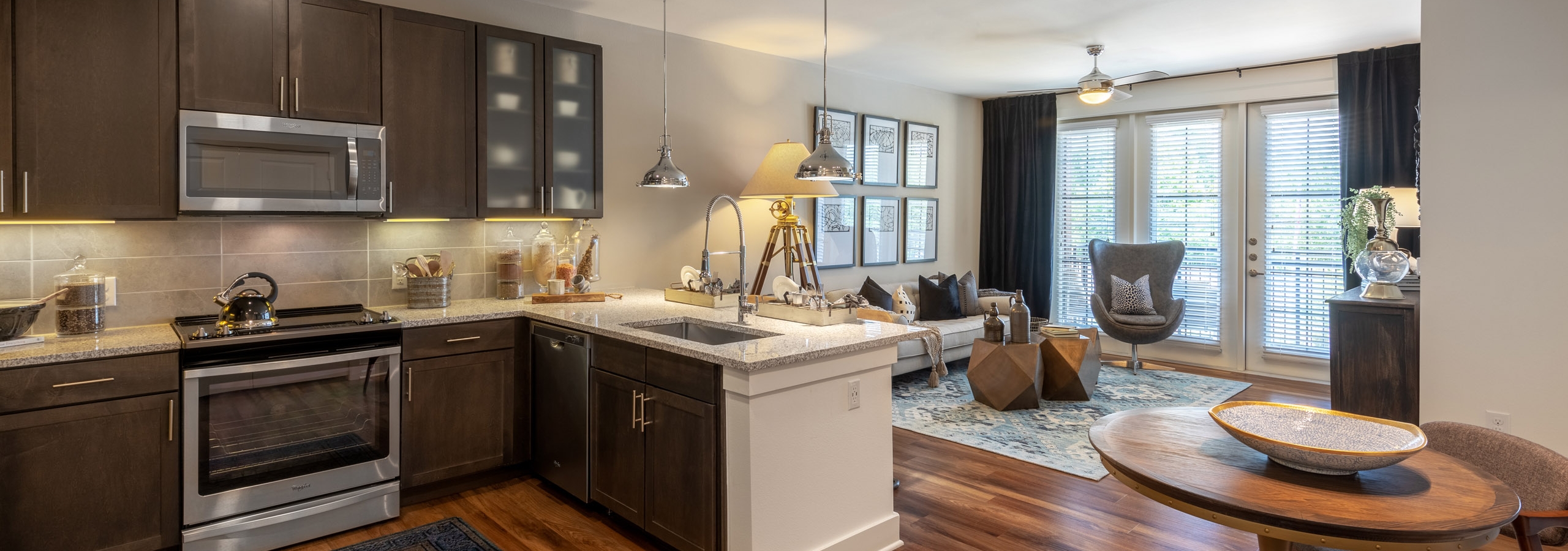 Interior view of AMLI Grapevine apartment kitchen and living room with dark cabinets and granite countertops and wood floors