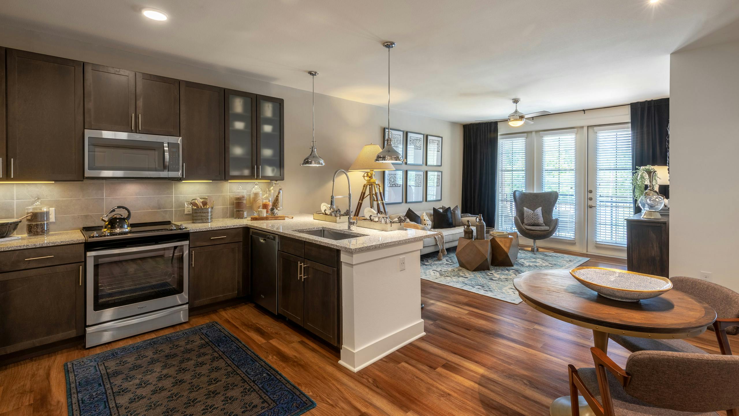 Interior view of AMLI Grapevine apartment kitchen and living room with dark cabinets and granite countertops and wood floors