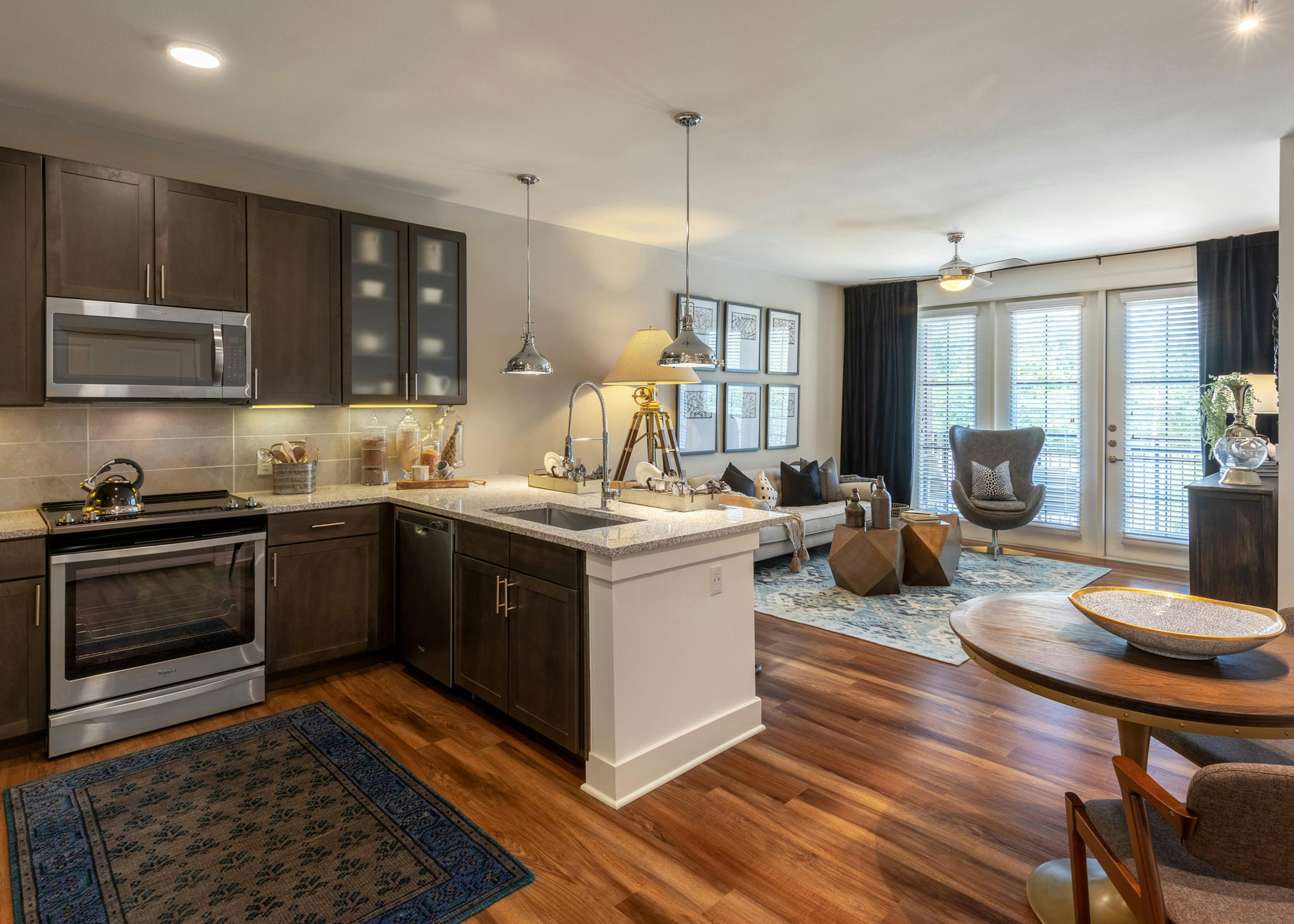 Interior view of AMLI Grapevine apartment kitchen and living room with dark cabinets and granite countertops and wood floors