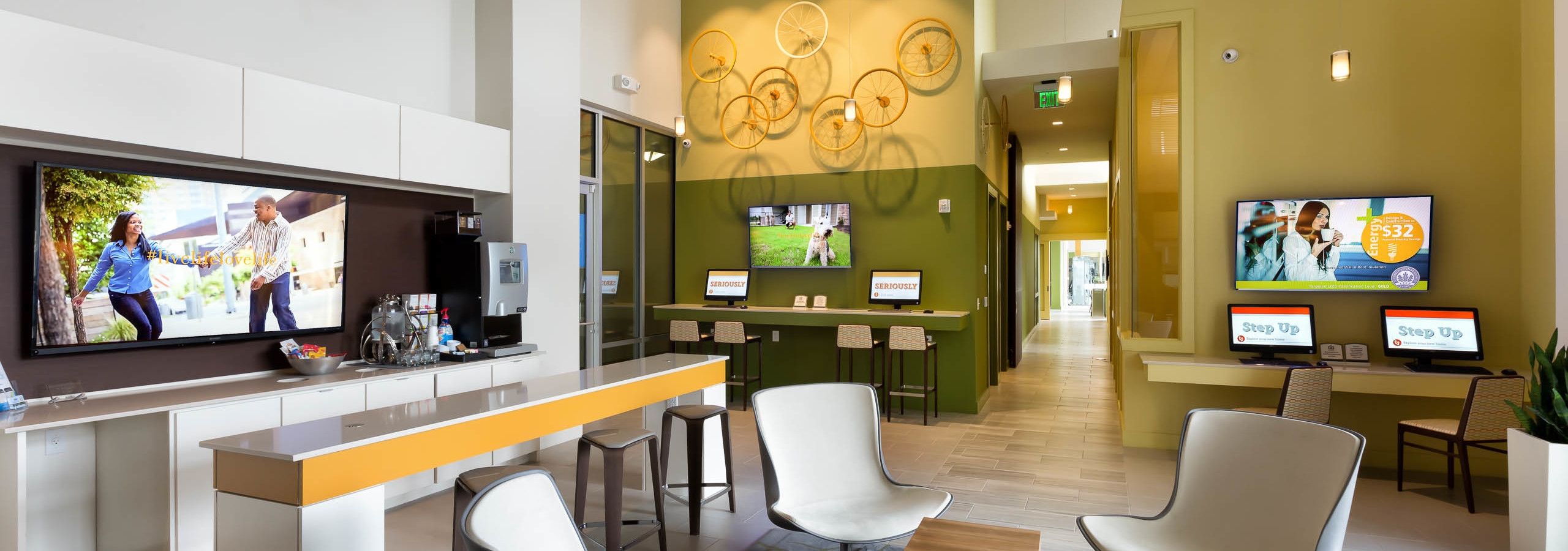 AMLI at Mueller leasing office with white chairs and a mustard accent wall featuring multiple computers and large TVs