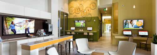 AMLI at Mueller leasing office with white chairs and a mustard accent wall featuring multiple computers and large TVs