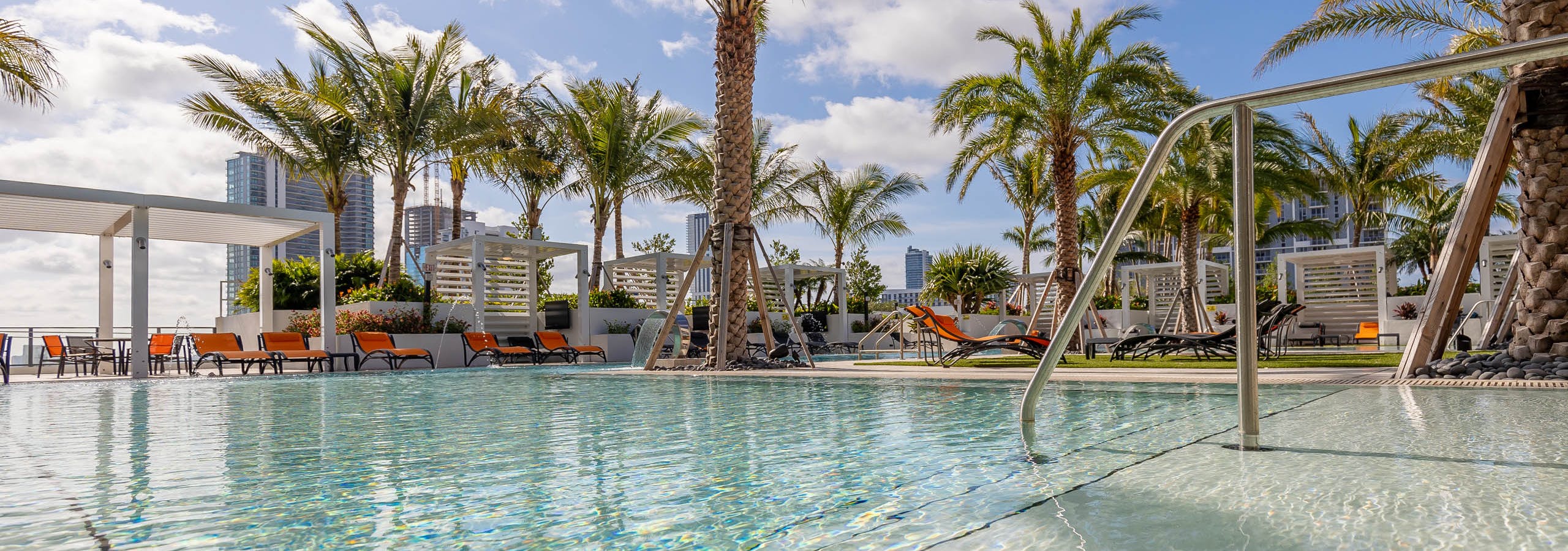 Sky view of AMLI Midtown Miami apartments pool overlooking the city with reflective water and lush palms and lounge chairs