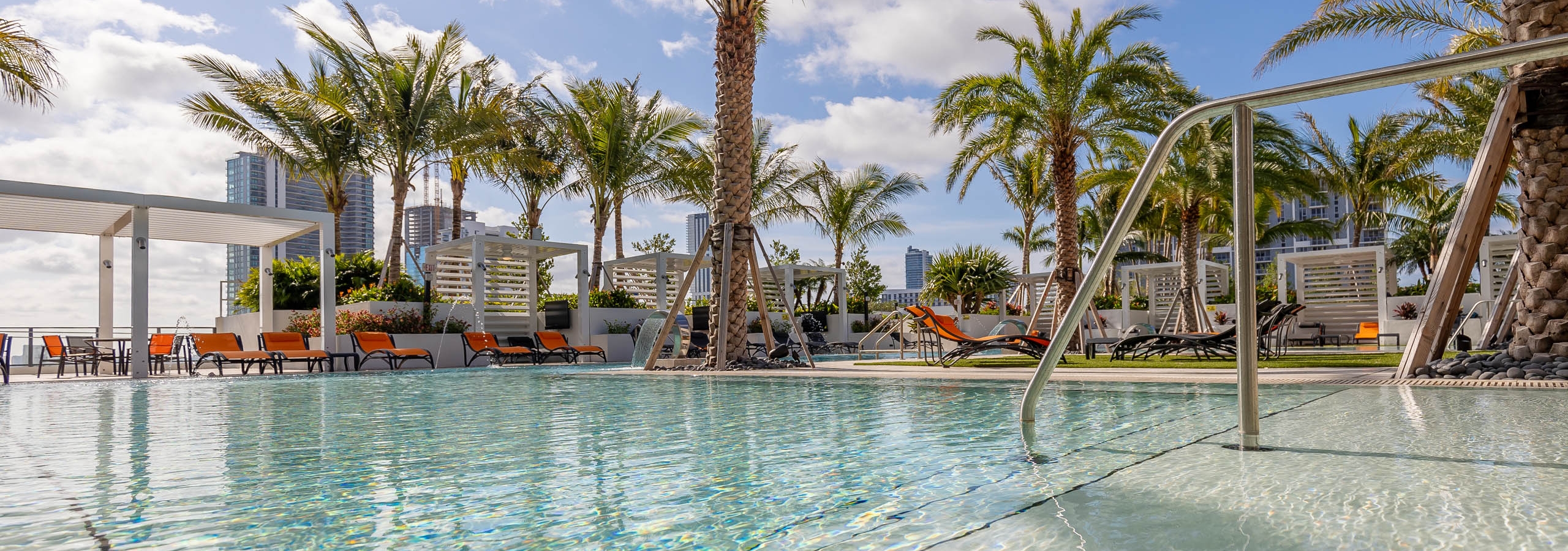 Sky view of AMLI Midtown Miami apartments pool overlooking the city with reflective water and lush palms and lounge chairs