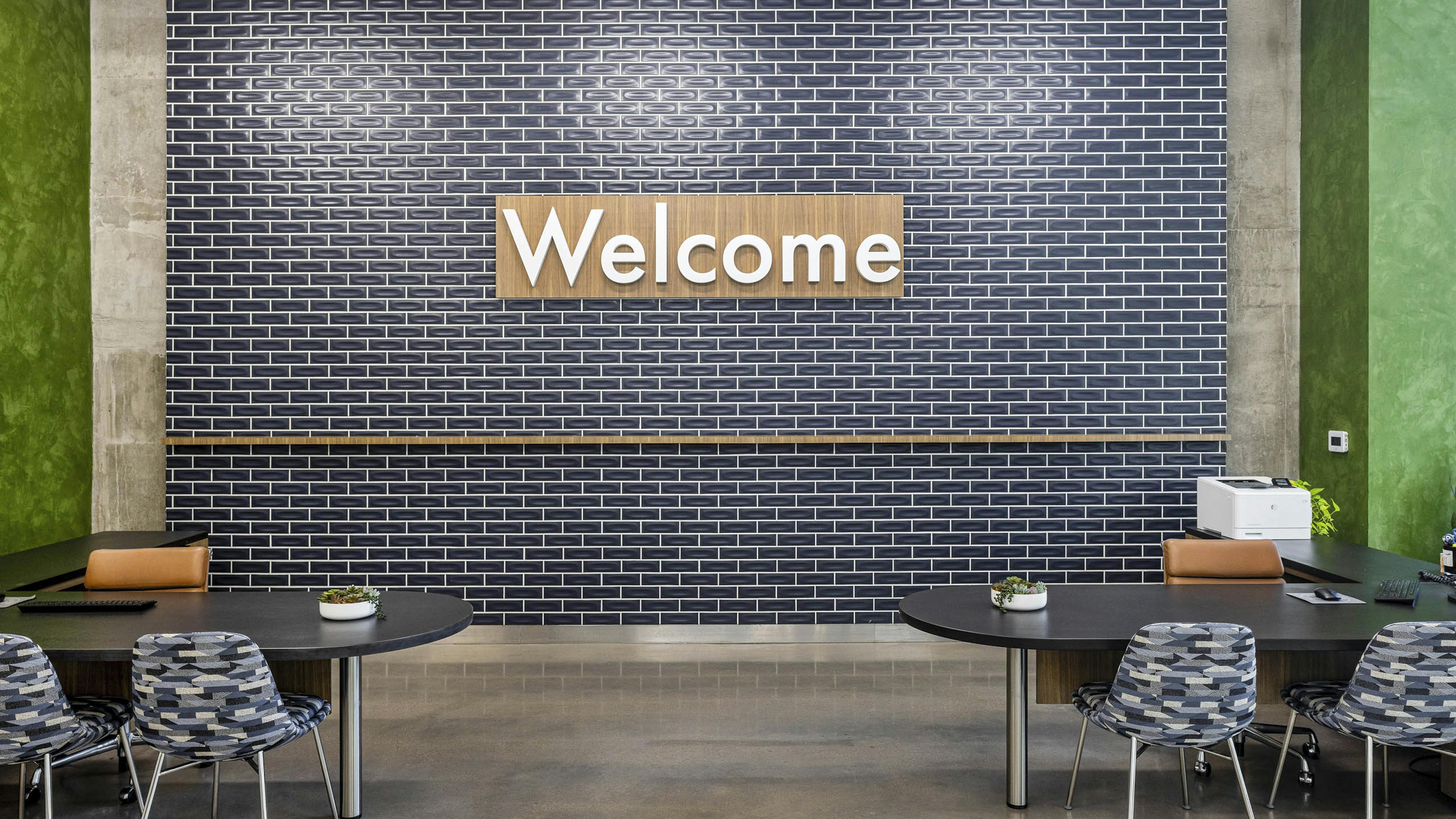 AMLI on 2nd leasing office with blue tile wall and wood welcome sign over 2 black desks with chairs with geometric fabric