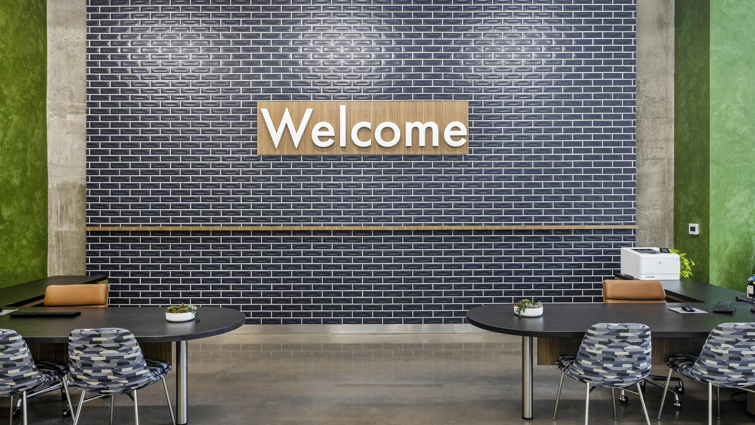 AMLI on 2nd leasing office with blue tile wall and wood welcome sign over 2 black desks with chairs with geometric fabric