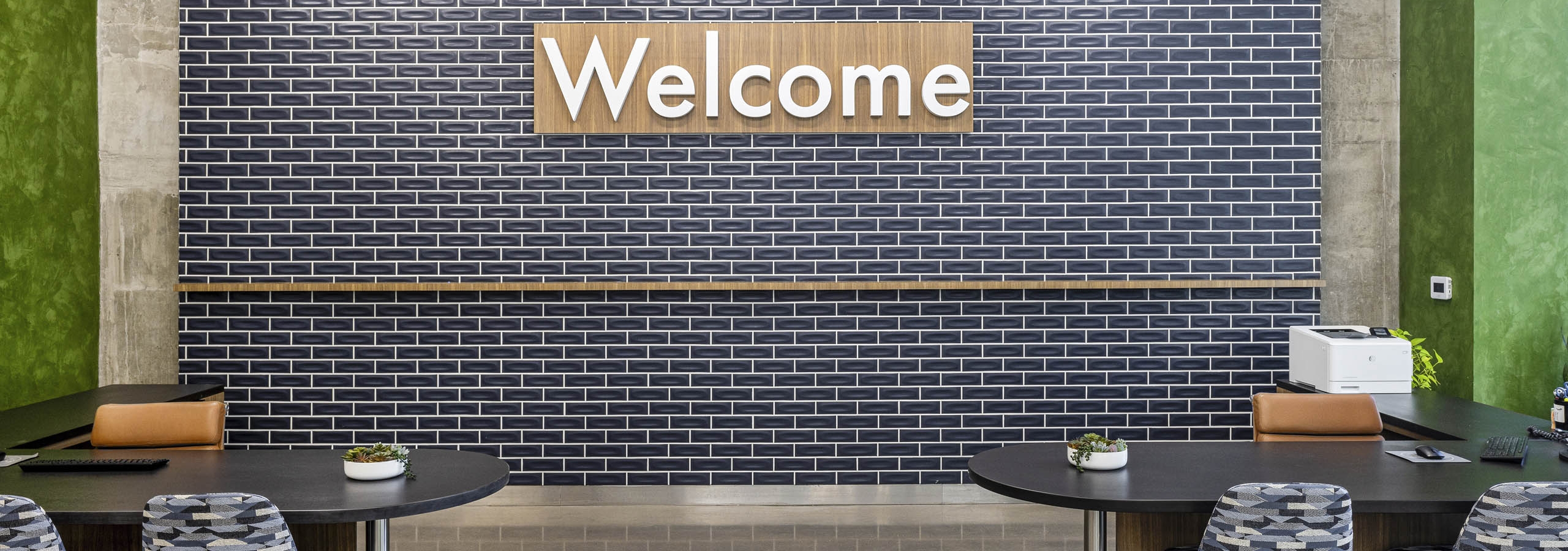 AMLI on 2nd leasing office with blue tile wall and wood welcome sign over 2 black desks with chairs with geometric fabric