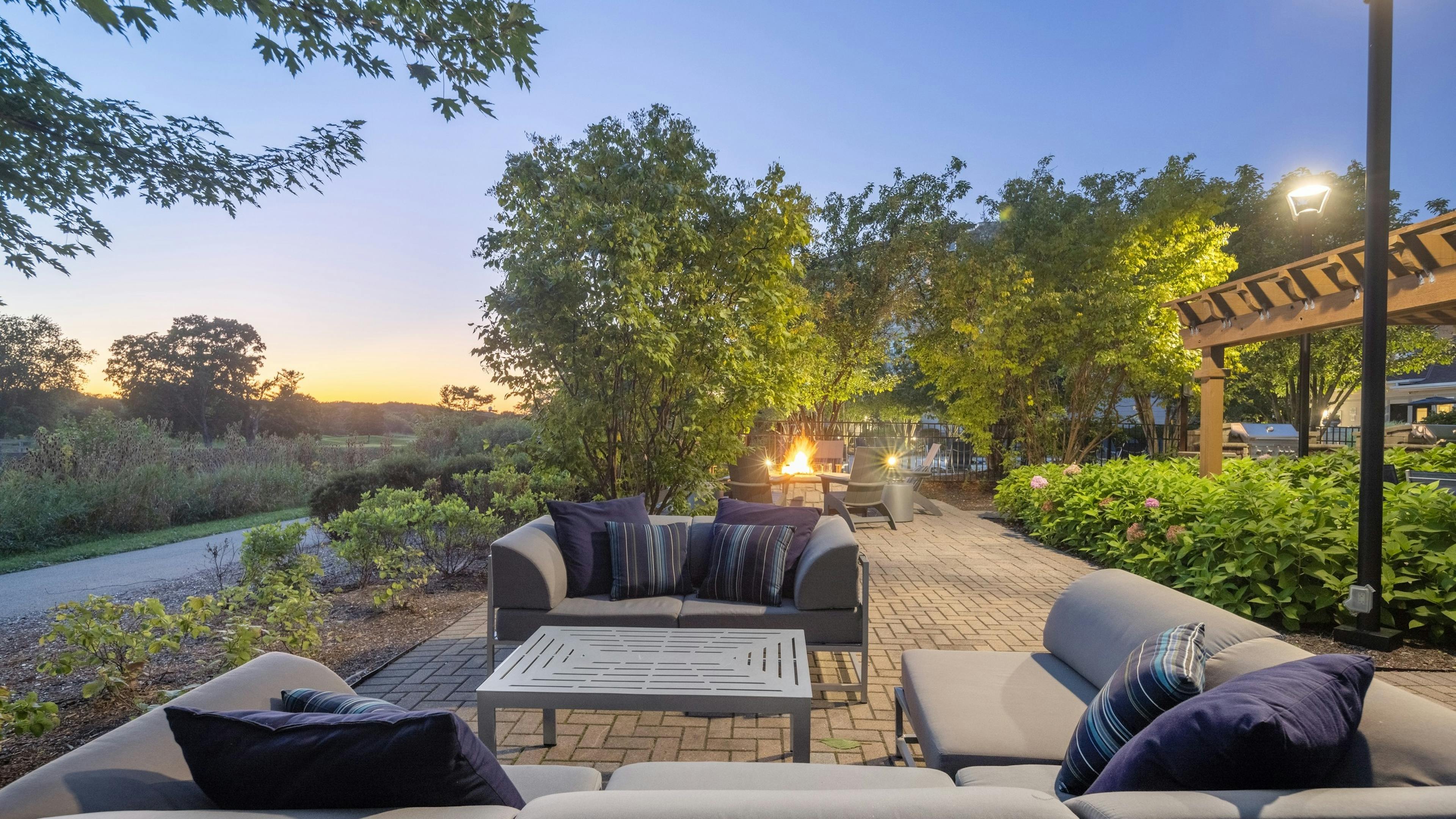AMLI at Seven Bridges outdoor lounge with couches and fire pit surround by plants and trees and overlooking golf course
