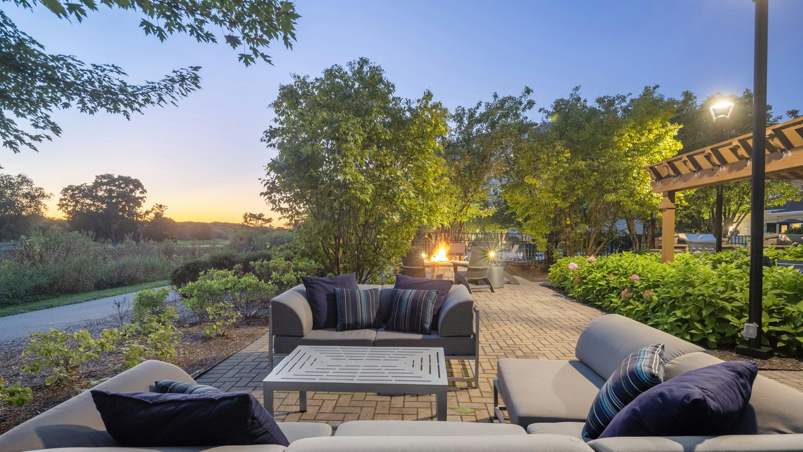 AMLI at Seven Bridges outdoor lounge with couches and fire pit surround by plants and trees and overlooking golf course