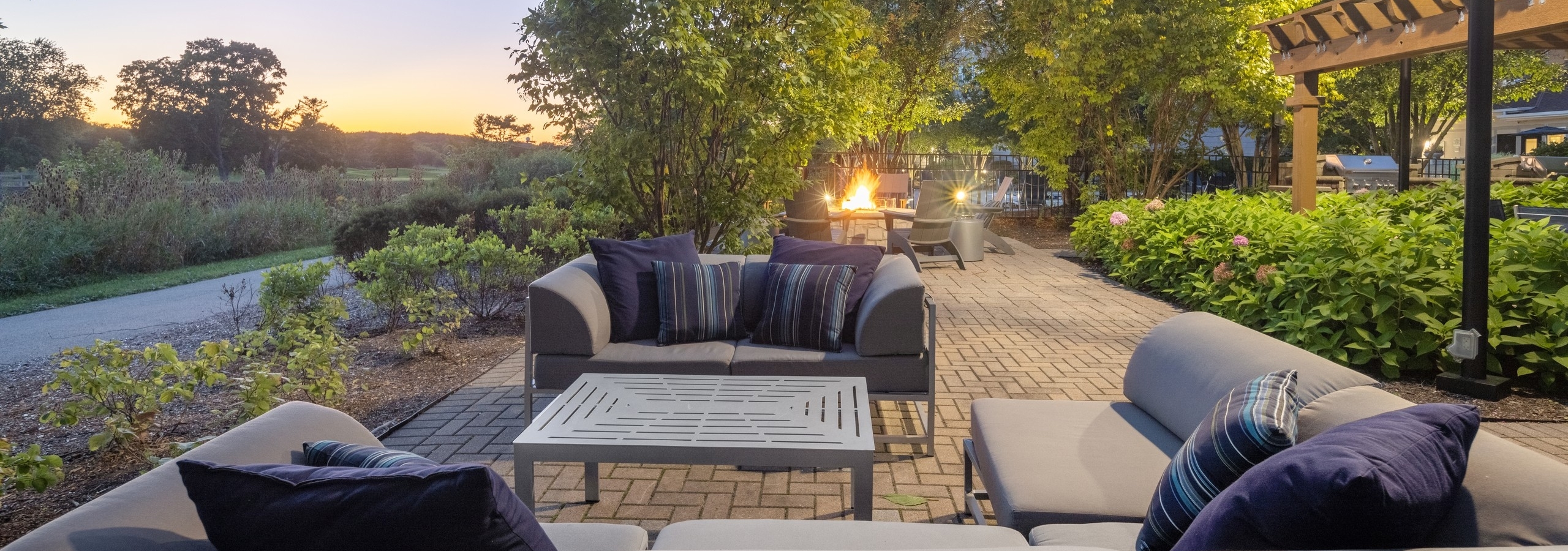 AMLI at Seven Bridges outdoor lounge with couches and fire pit surround by plants and trees and overlooking golf course