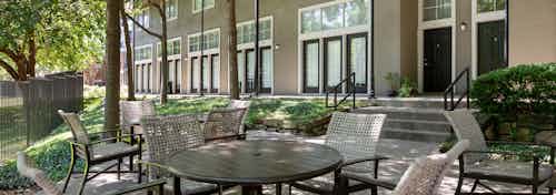 Daytime exterior view of tables and chairs in landscaped area outside of AMLI Memorial Heights apartment building
