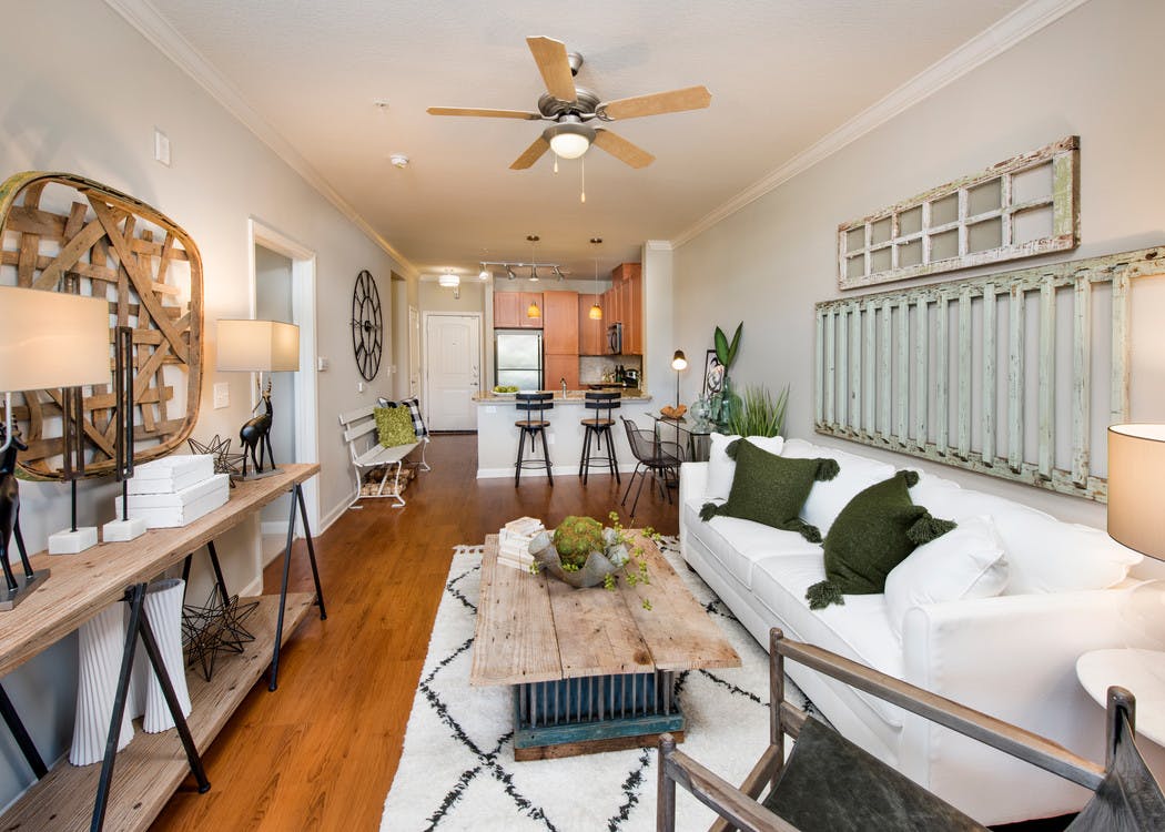 AMLI North Point living room with rustic decor and medium colored wood floors which connect to kitchen area in the background