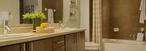 AMLI Uptown apartment bathroom with double vanity, large mirror, dark wood cabinets and garden tub with tile surround