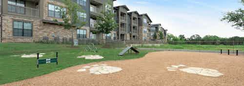 Daytime view of AMLI Covered Bridge fenced dog park with a wood chipper play area and a dog playground with grass lawn