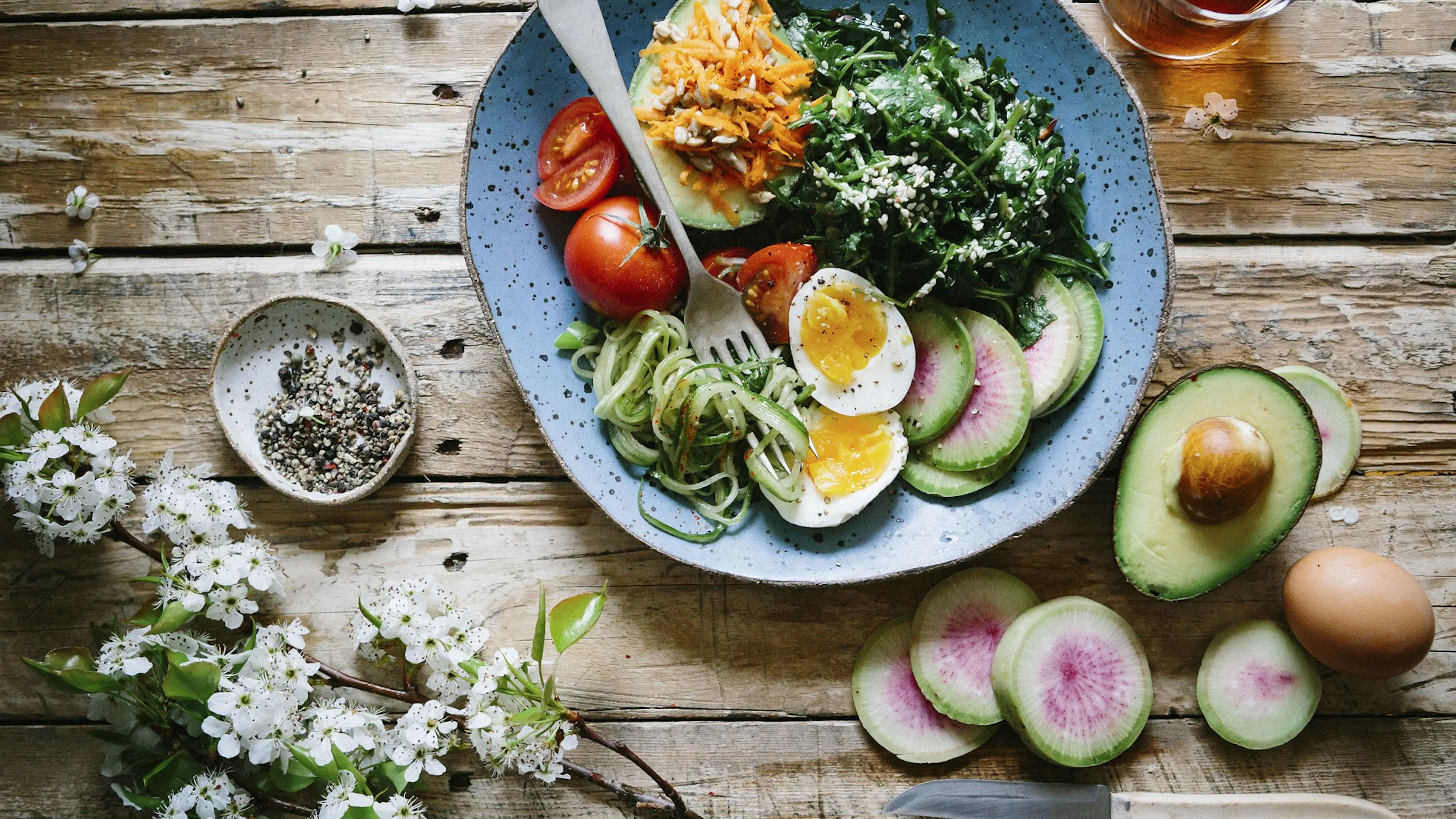 Salad in bowl with flowers and avocado on wood boards