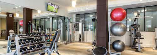 AMLI West Plano fitness center showing dumbbell rack with large TV hanging on the wall with weight machines in the background