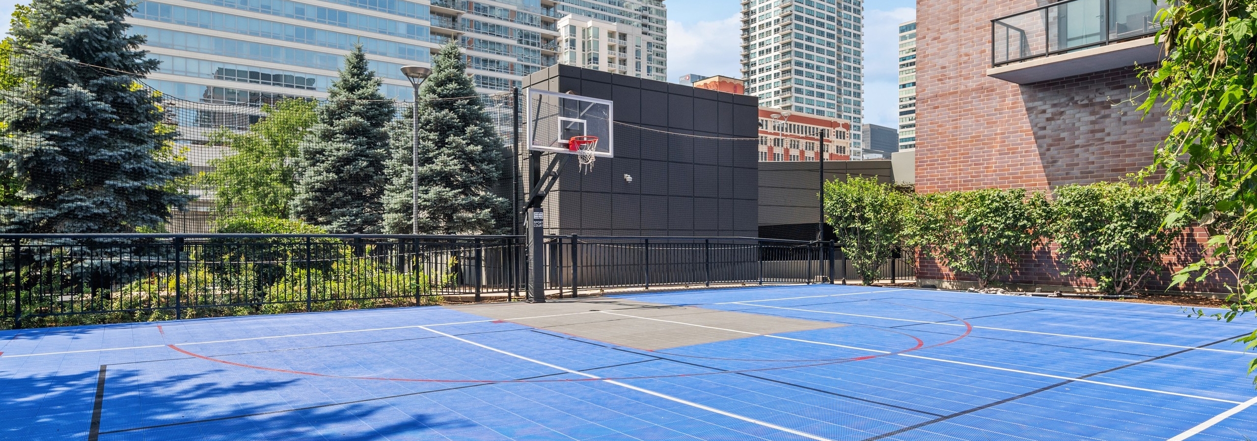 Outside view of AMLI Lofts sport court with blue tile flooring and basketball hoop with city buildings visible in background