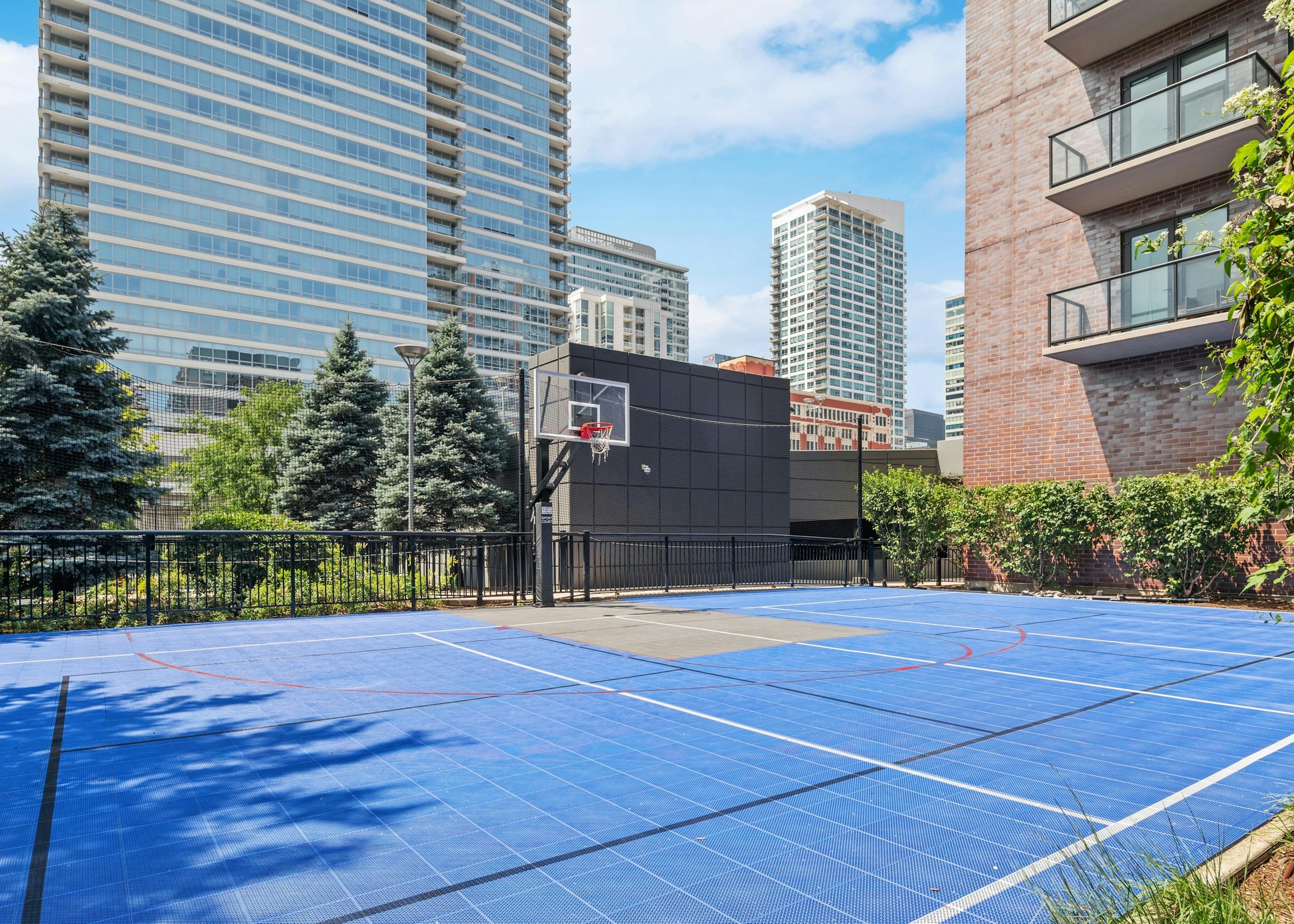 Outside view of AMLI Lofts sport court with blue tile flooring and basketball hoop with city buildings visible in background