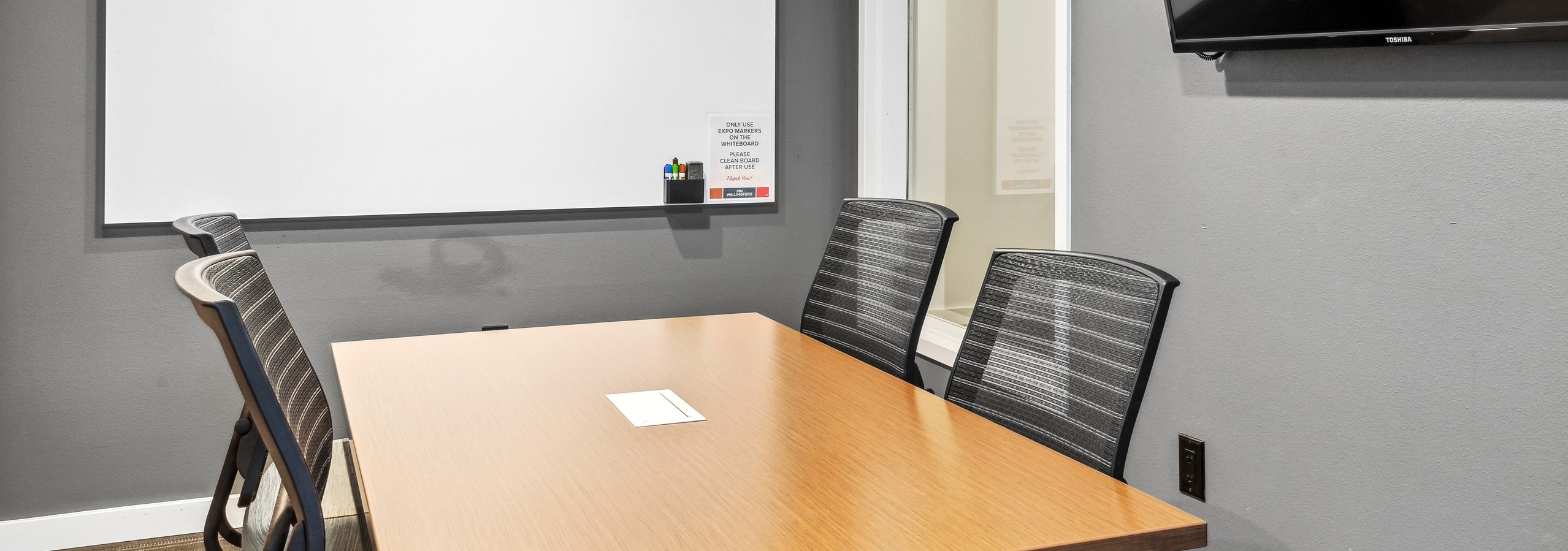 Interior view of a conference room at AMLI Wallingford with a table and 4 chairs and a dry erase board and a TV