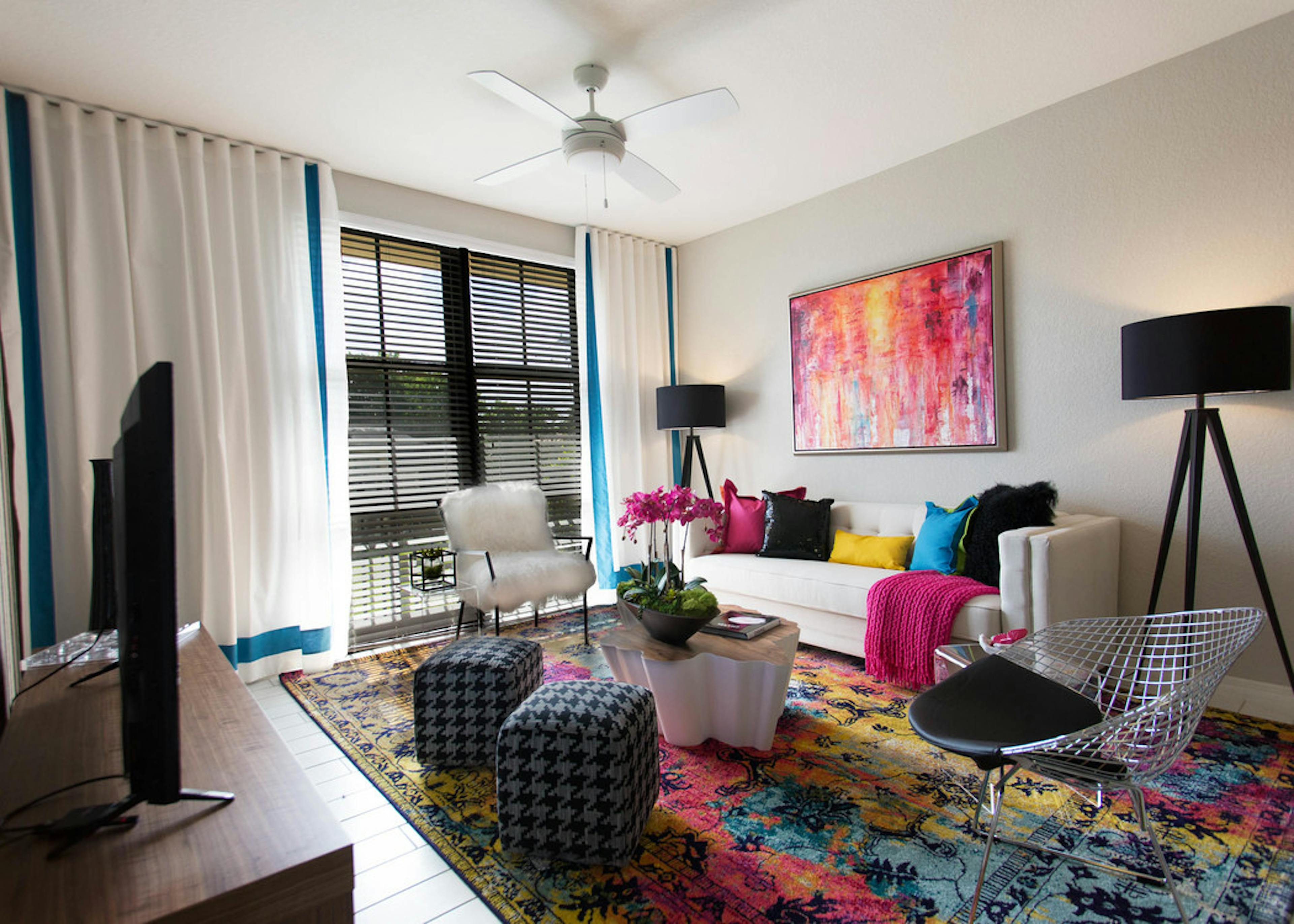 Interior of an AMLI Dadeland apartment living area with white sofa, pillows, modern colorful artwork and black floor lamps 