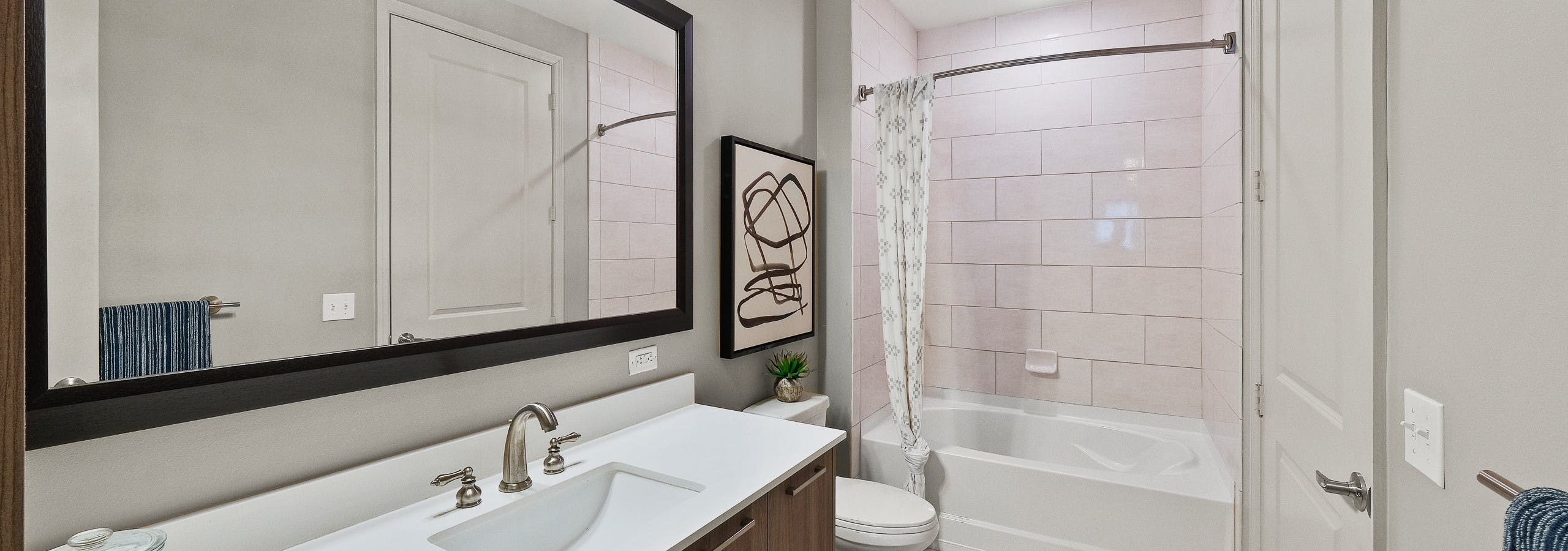 Interior view of AMLI 8800 apartment bathroom with large single vanity, sink with faucet, mirror, toilet and soaking tub
