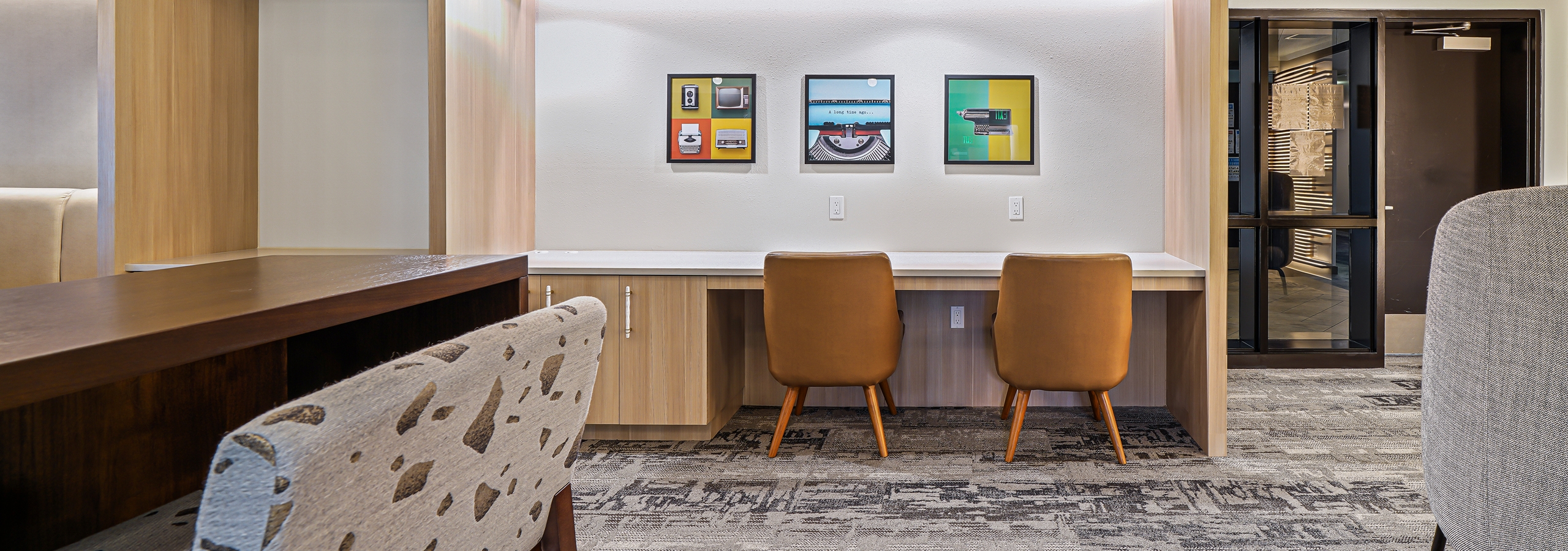 Interior view of AMLI Bellevue Park business center with gray carpet and 2 brown chairs at desk and wood slat ceiling