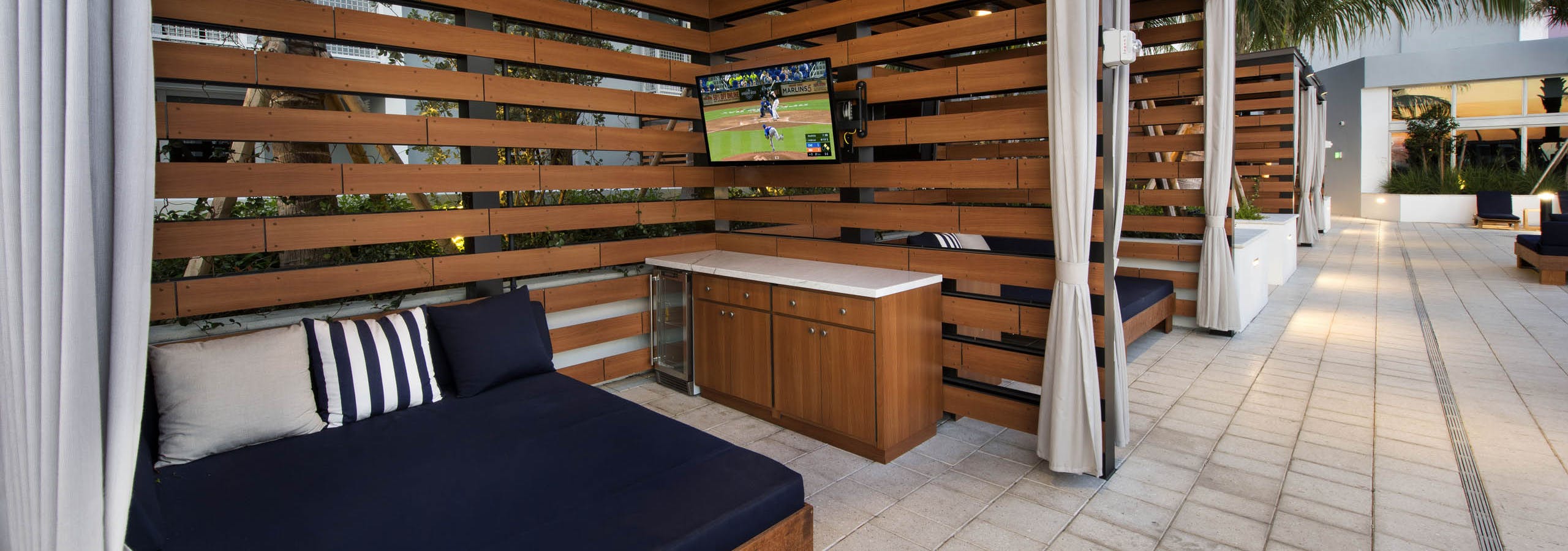 View of wood slat cabanas with oversized blue lounge and bar area with mini-fridge and TV at AMLI Midtown 29 apartments
