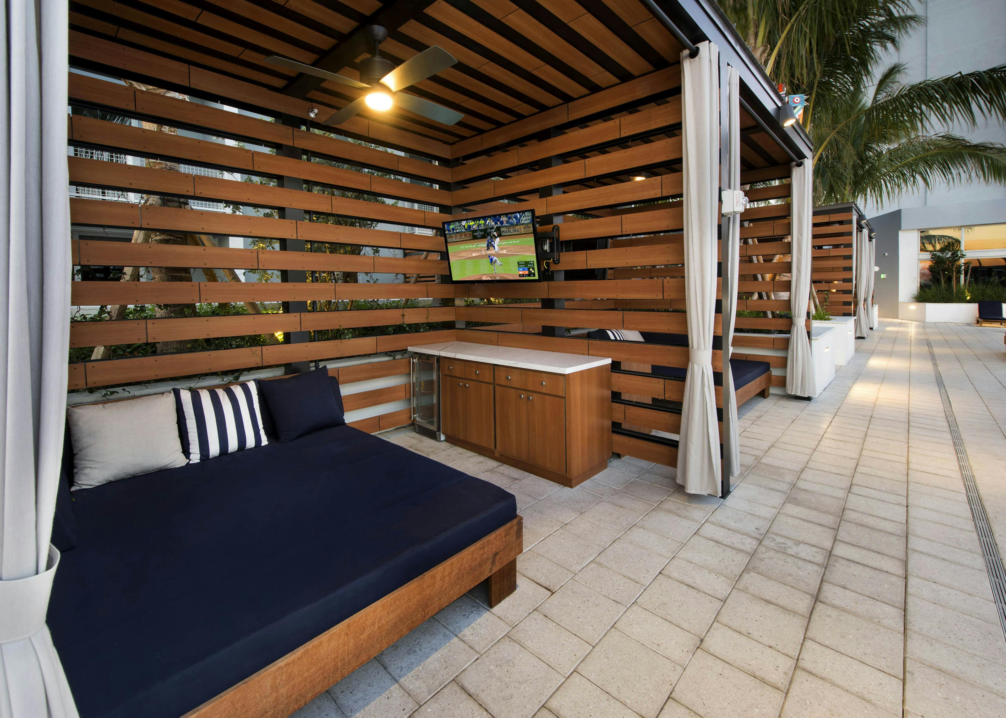 View of wood slat cabanas with oversized blue lounge and bar area with mini-fridge and TV at AMLI Midtown 29 apartments