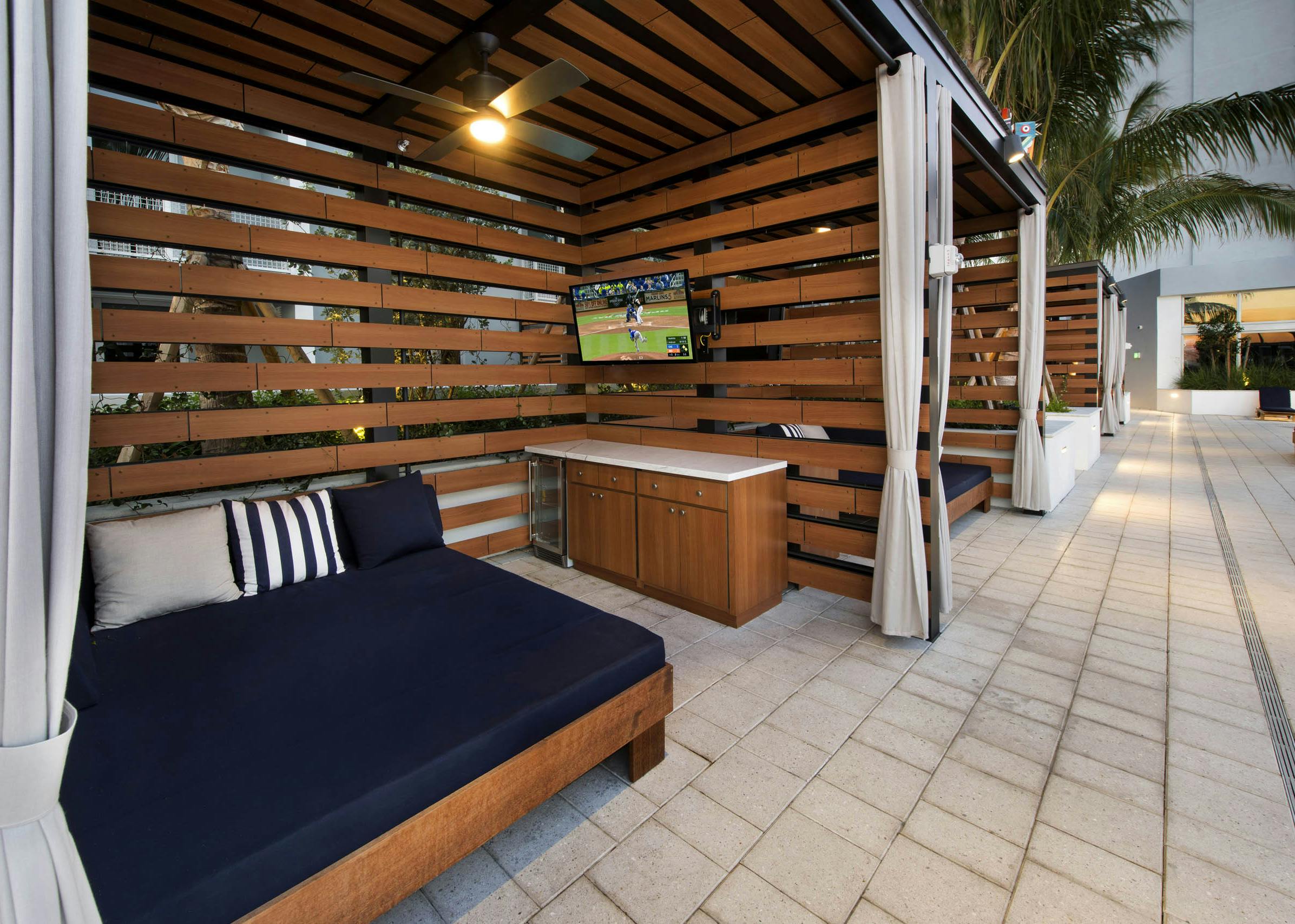 View of wood slat cabanas with oversized blue lounge and bar area with mini-fridge and TV at AMLI Midtown 29 apartments