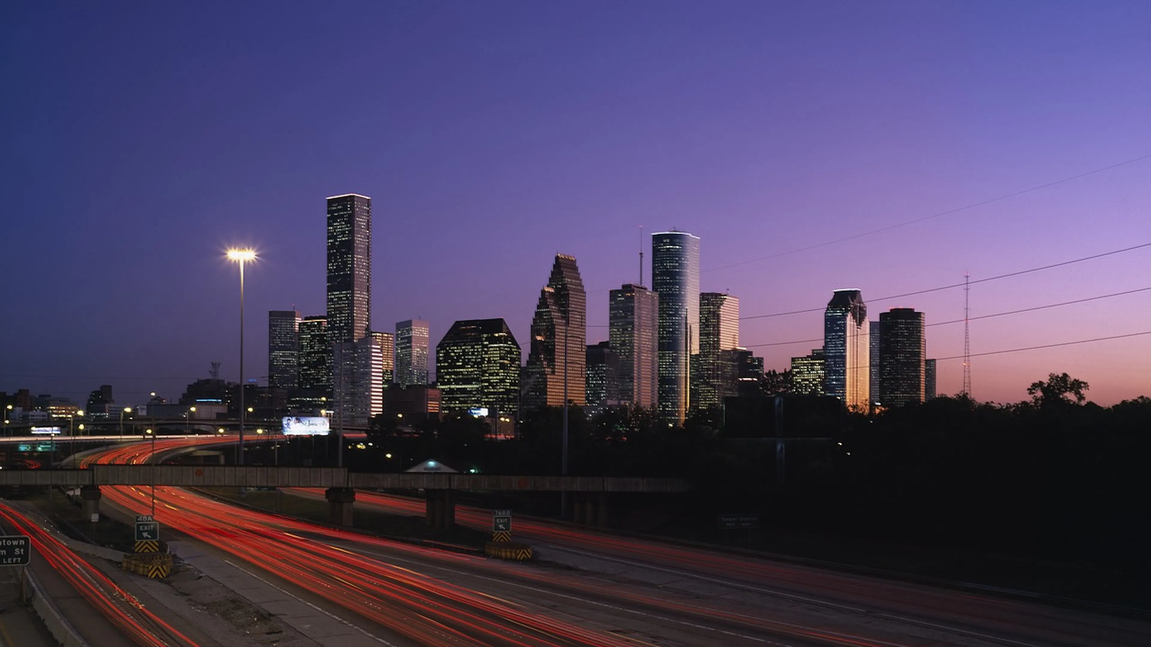 Houston's skyline at night with cars streaking past on the highway