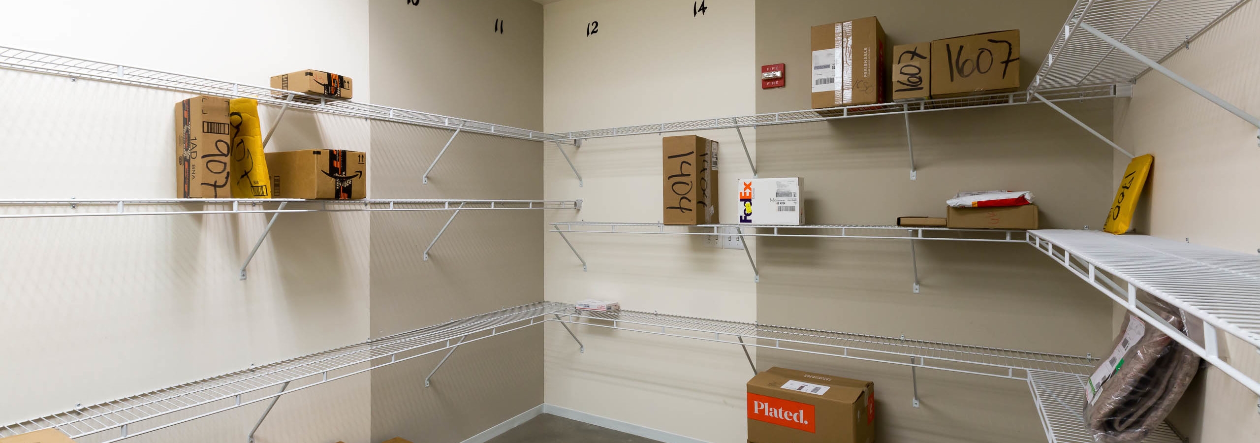 Interior view of package room at AMLI on 2nd with light walls and packages scattered along built in white shelving