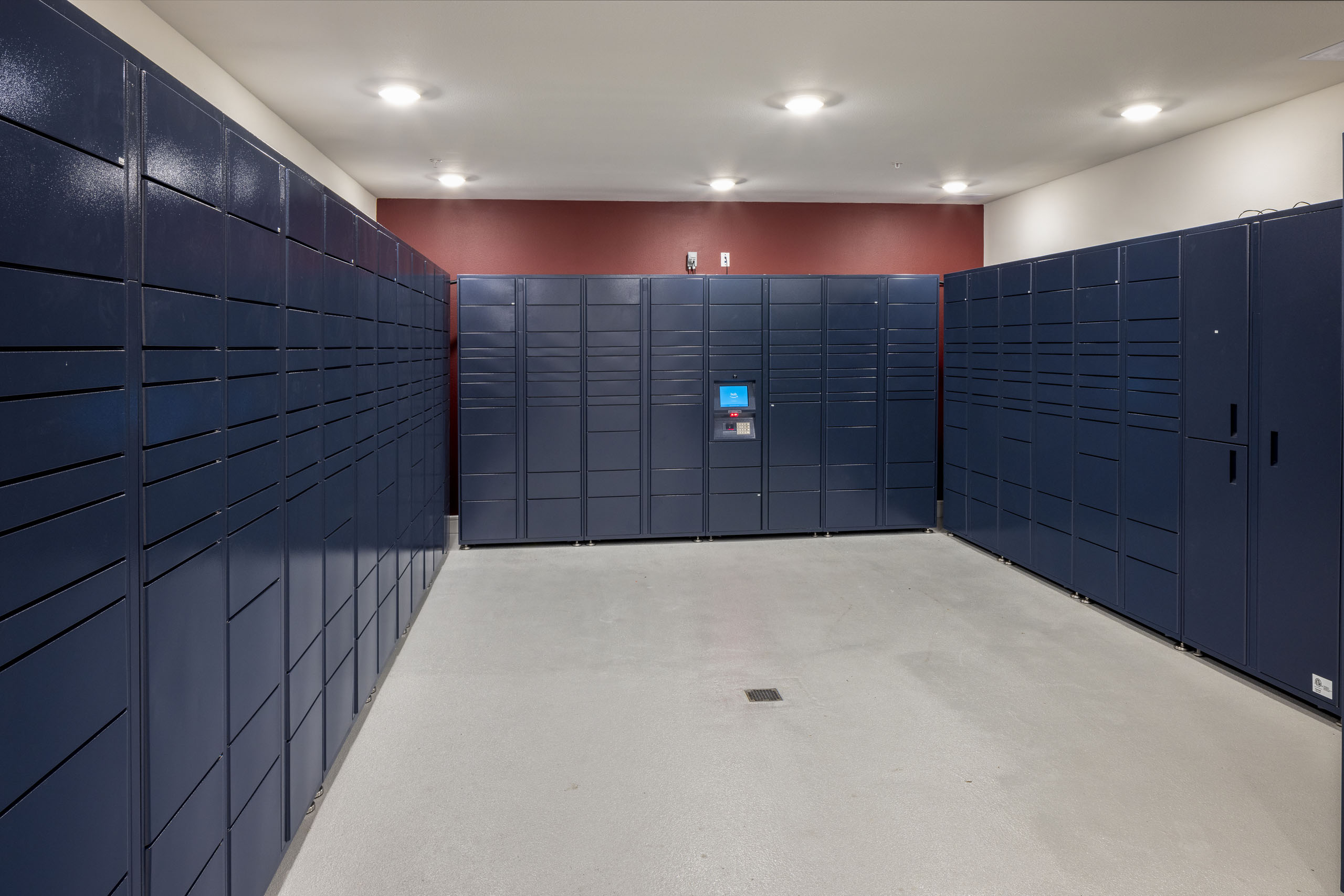 Interior view of package room at AMLI Lakeline with navy lockers lining the red and white walls with light gray flooring