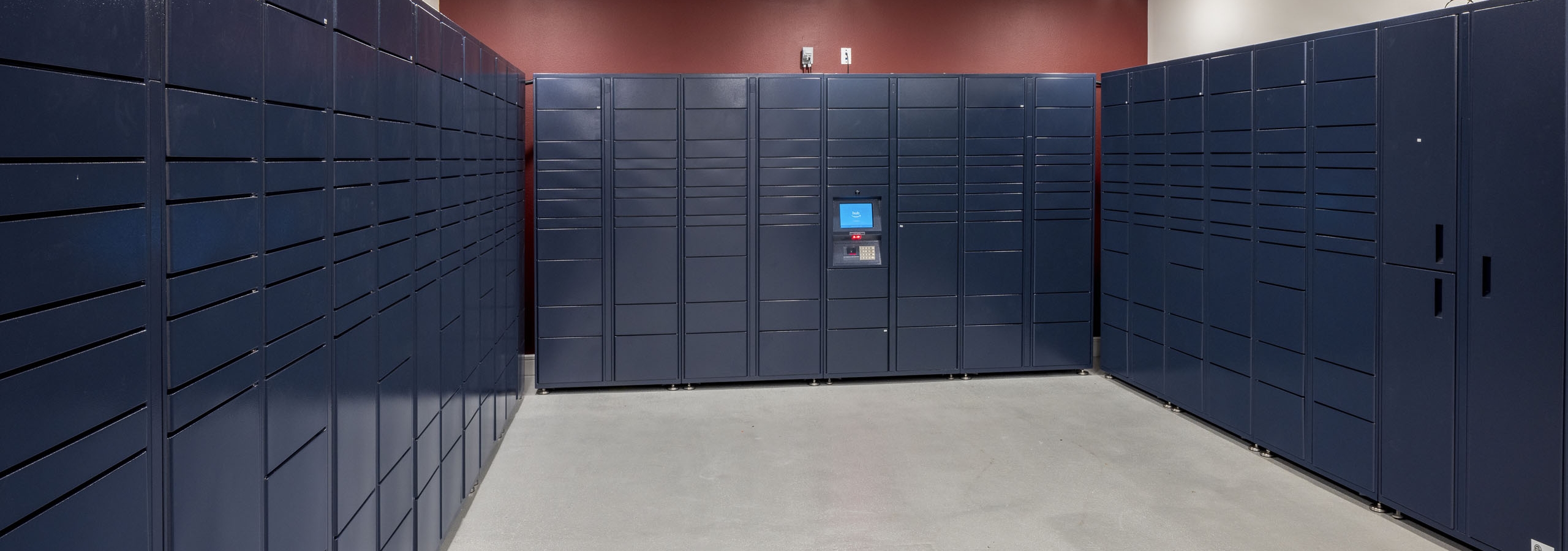Interior view of package room at AMLI Lakeline with navy lockers lining the red and white walls with light gray flooring