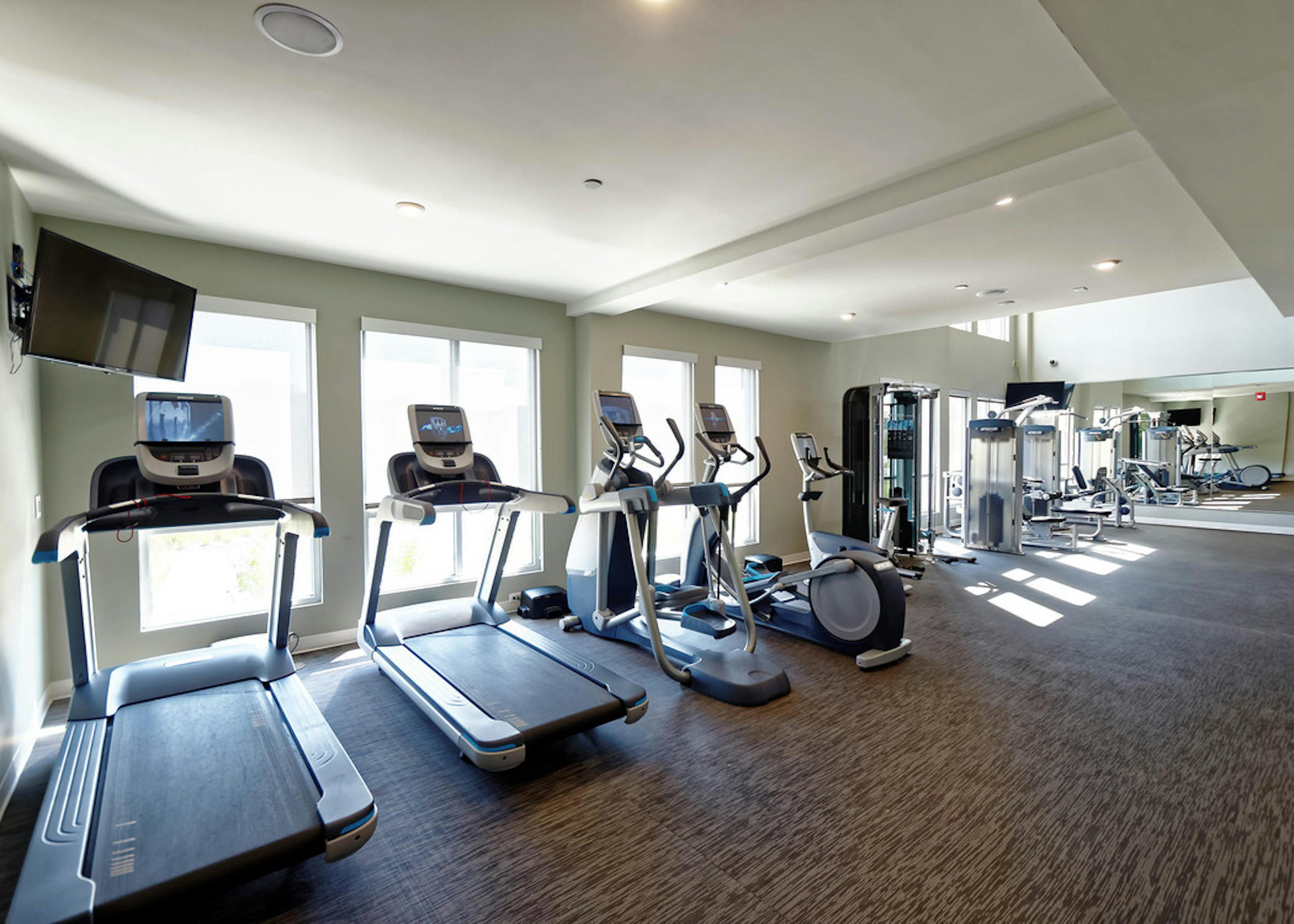 Interior view of fitness center at AMLI Dry Creek apartments with multiple treadmills and elliptical machines and windows